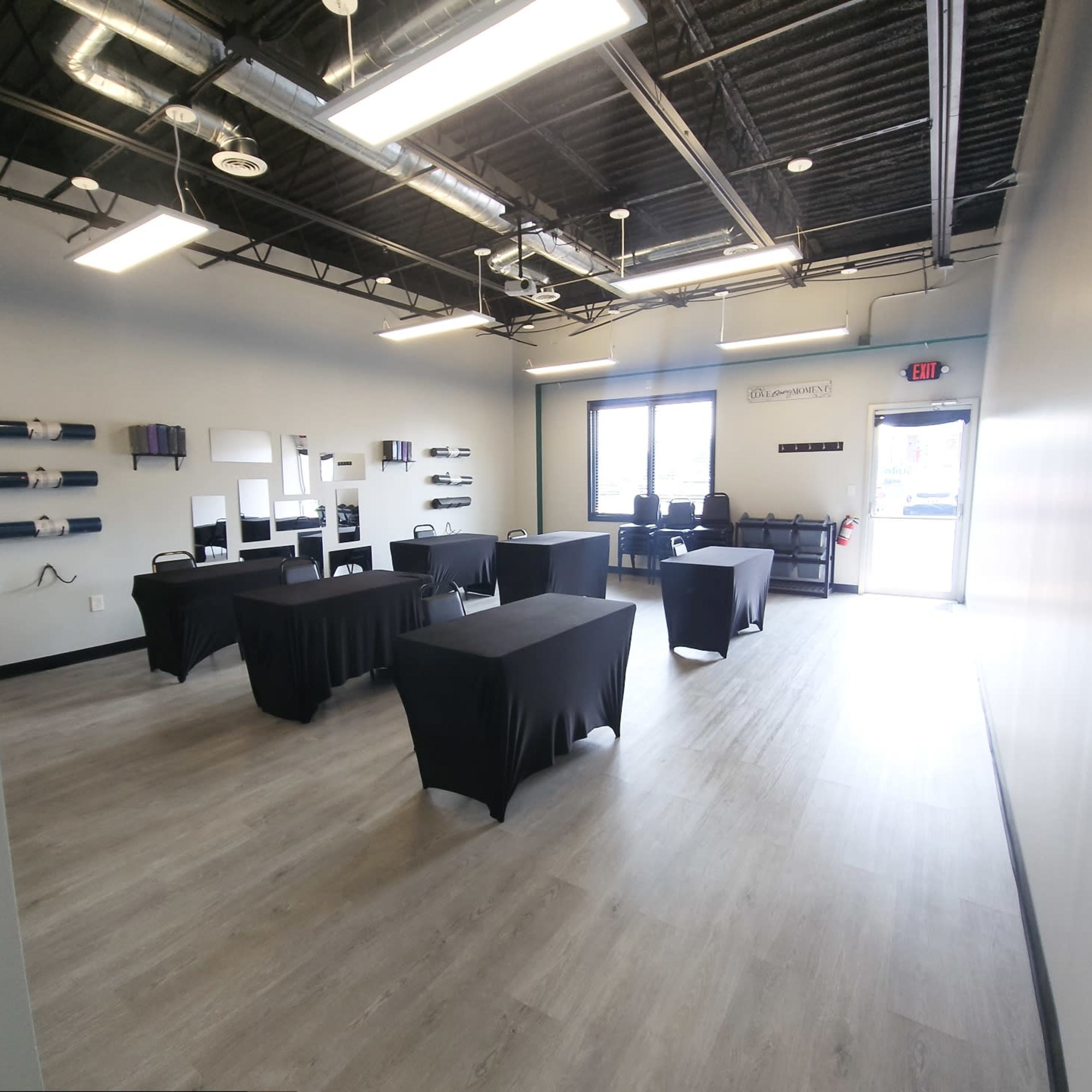A modern, empty room with several black tables arranged throughout and a door leading outside.