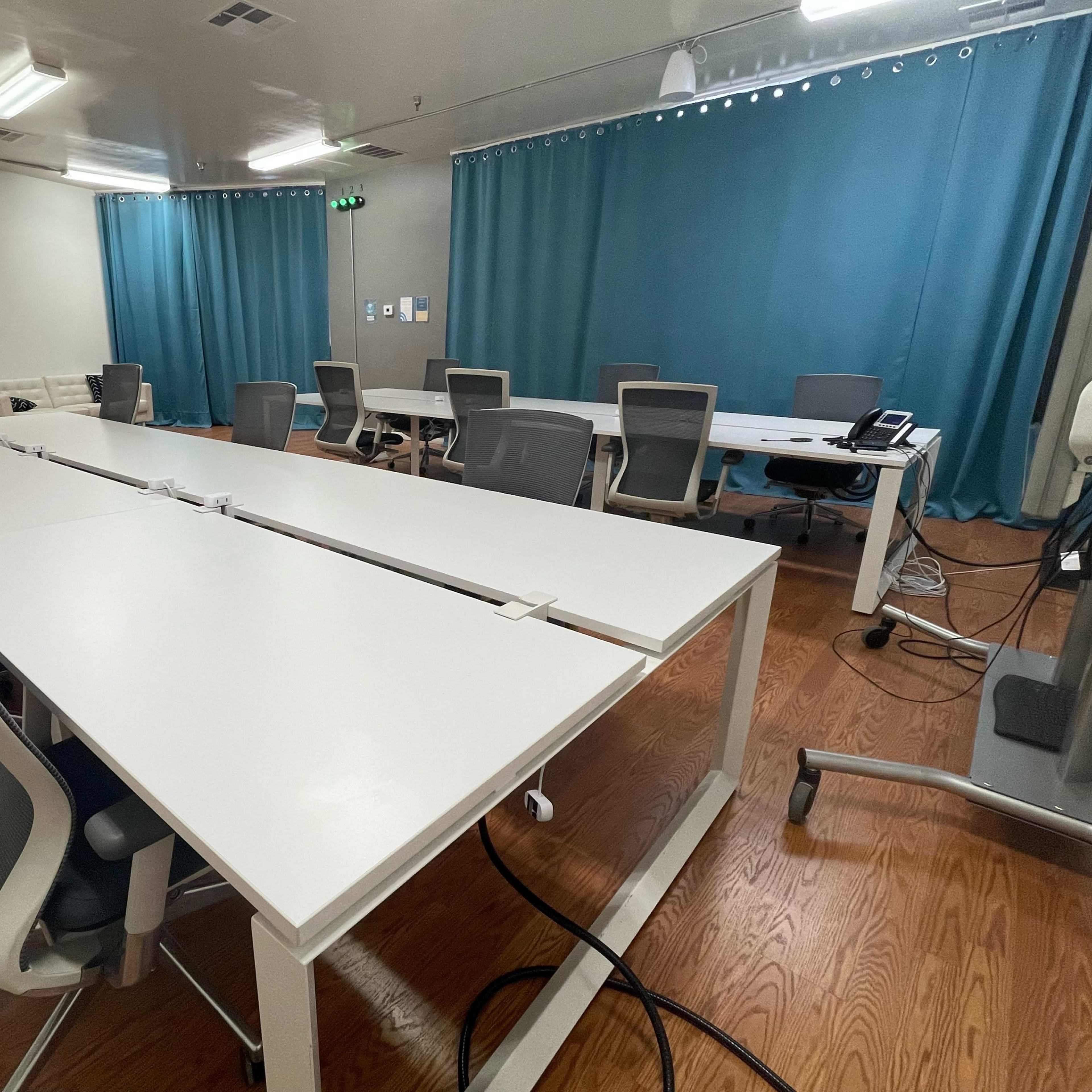 A modern conference room with multiple white tables and ergonomic chairs, separated by a blue curtain in the background.