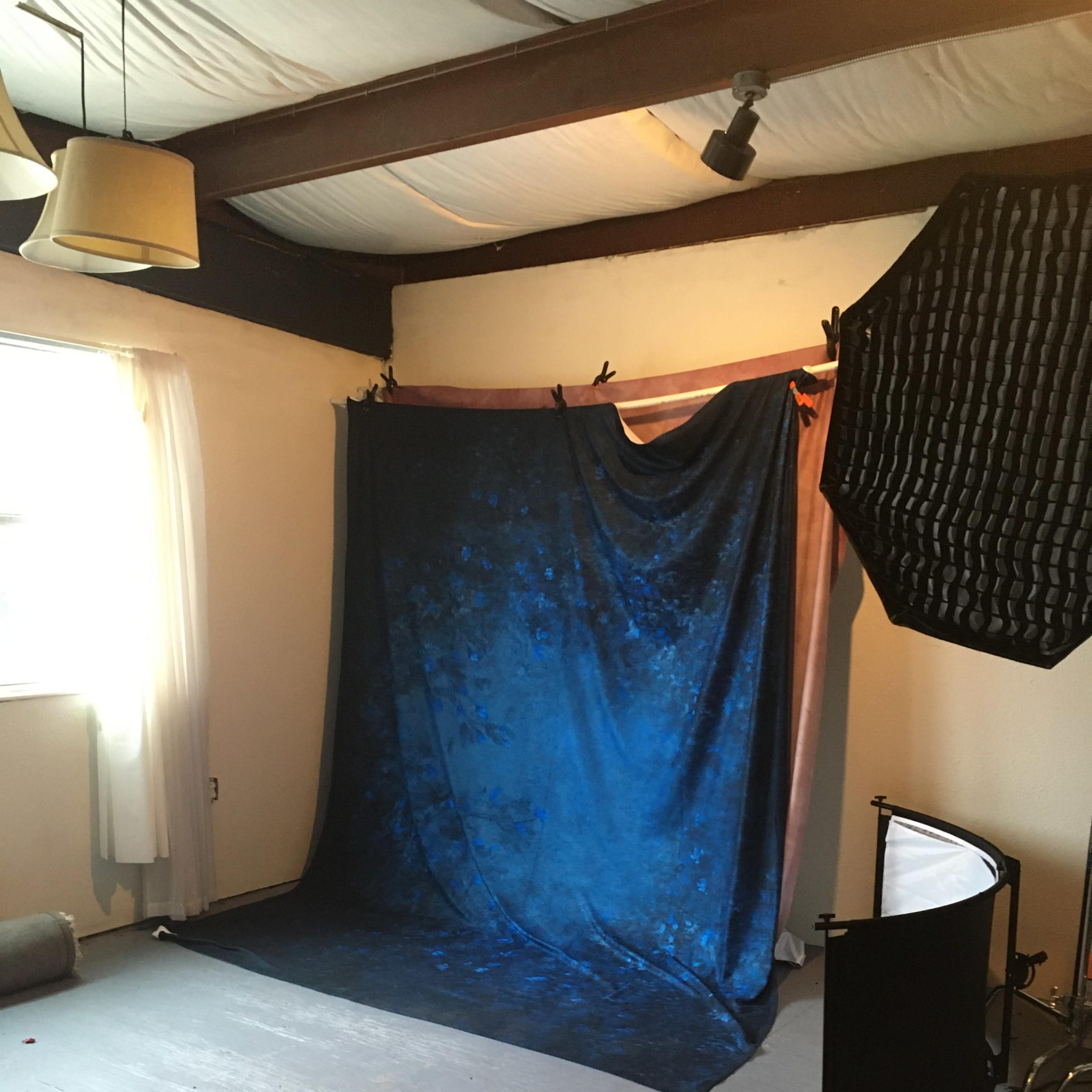 A photography studio setup featuring a blue backdrop, soft lighting equipment, and a light reflector.