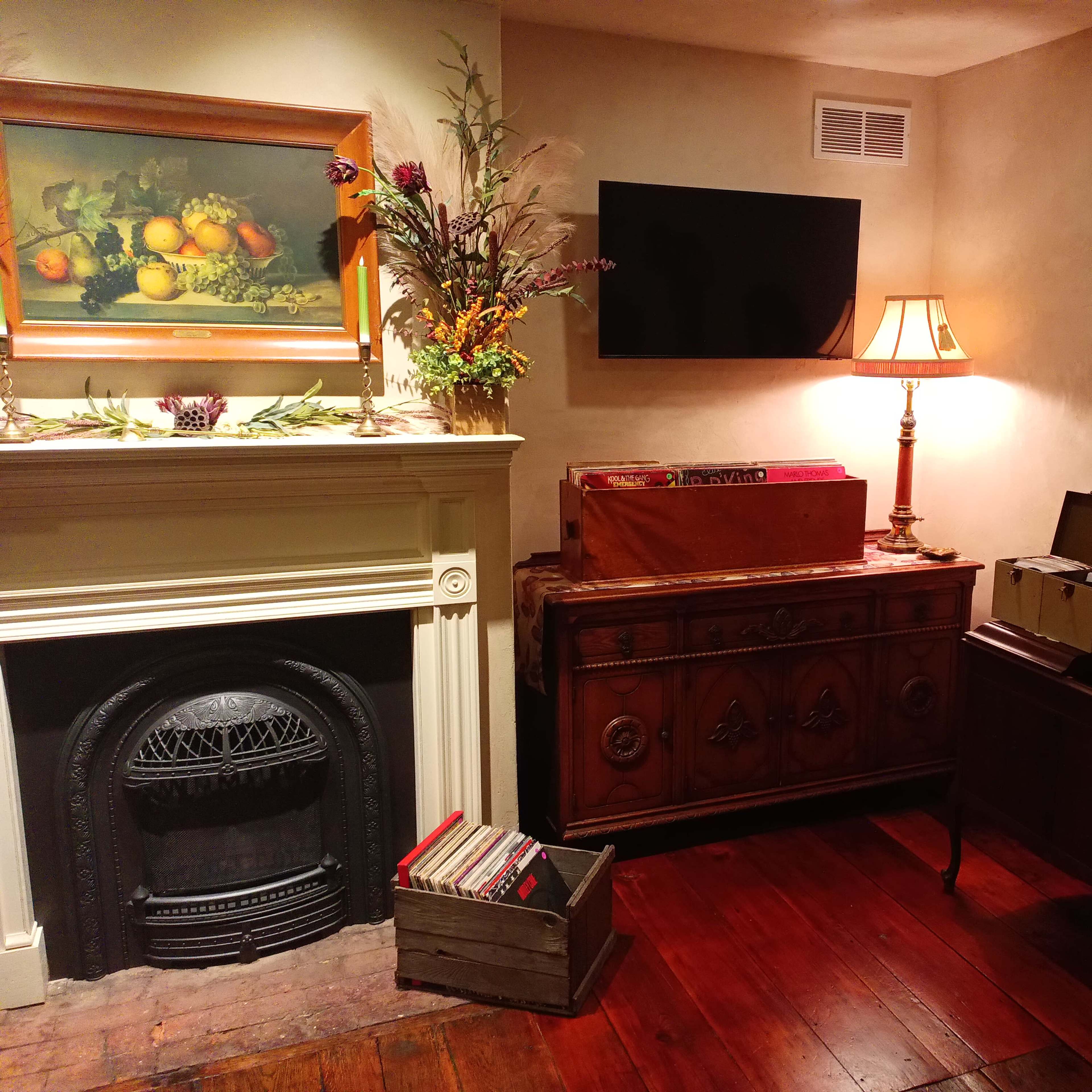 A cozy room featuring a fireplace, a wooden chest, a lamp, and a wall-mounted television.
