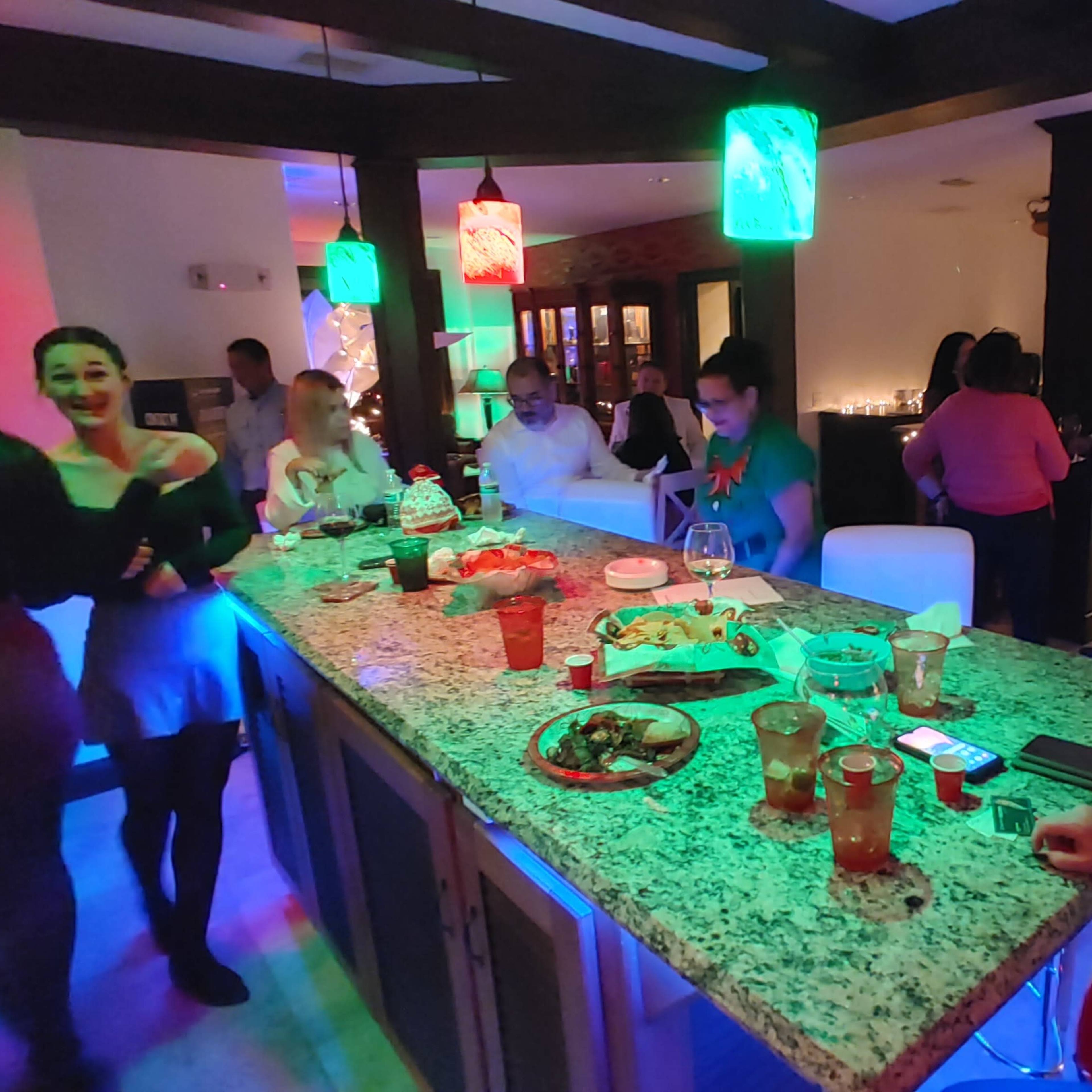 A lively bar scene is depicted, with patrons socializing and enjoying food and drinks under colorful lighting.
