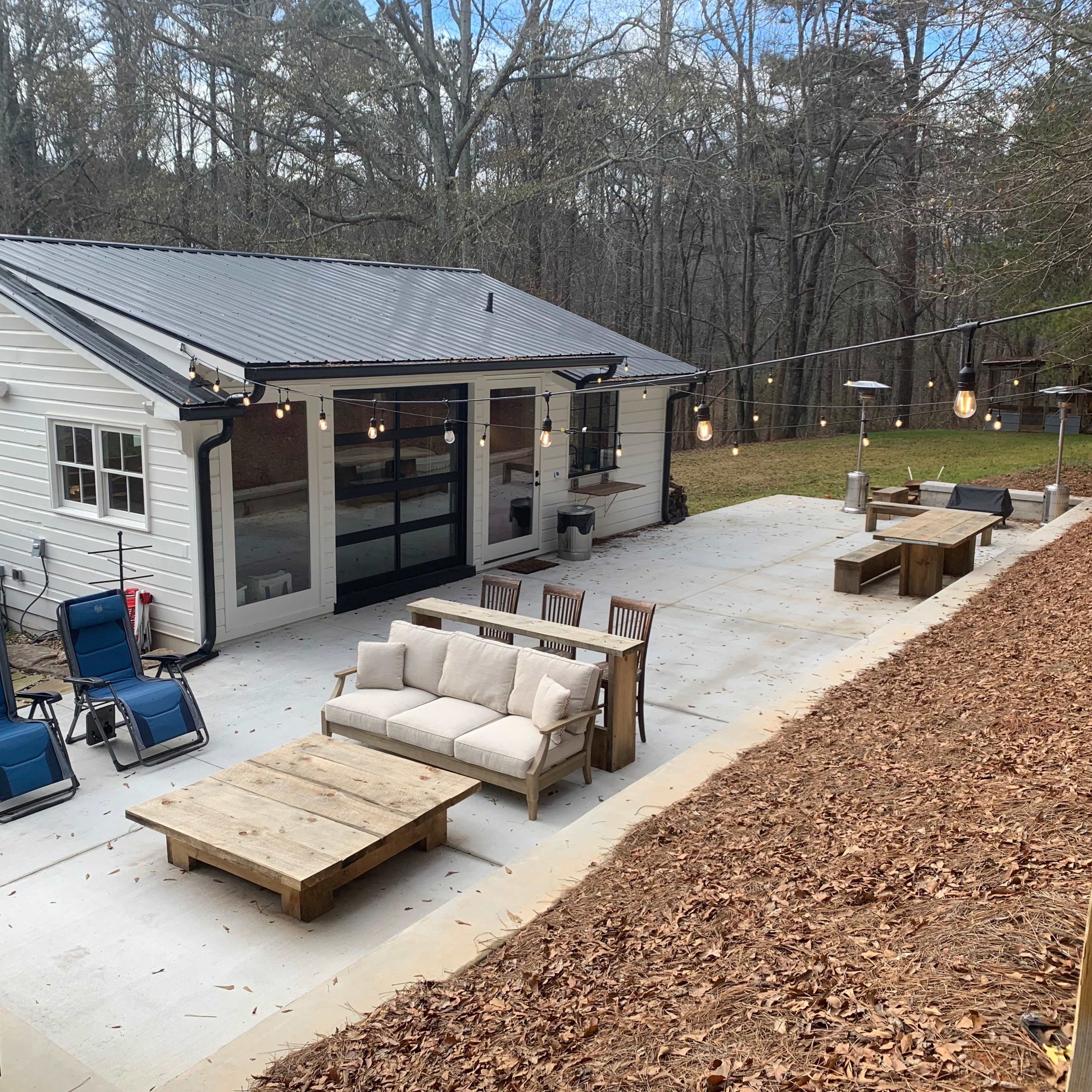 A backyard area features a modern cabin, outdoor seating with a coffee table, and string lights illuminating the space.