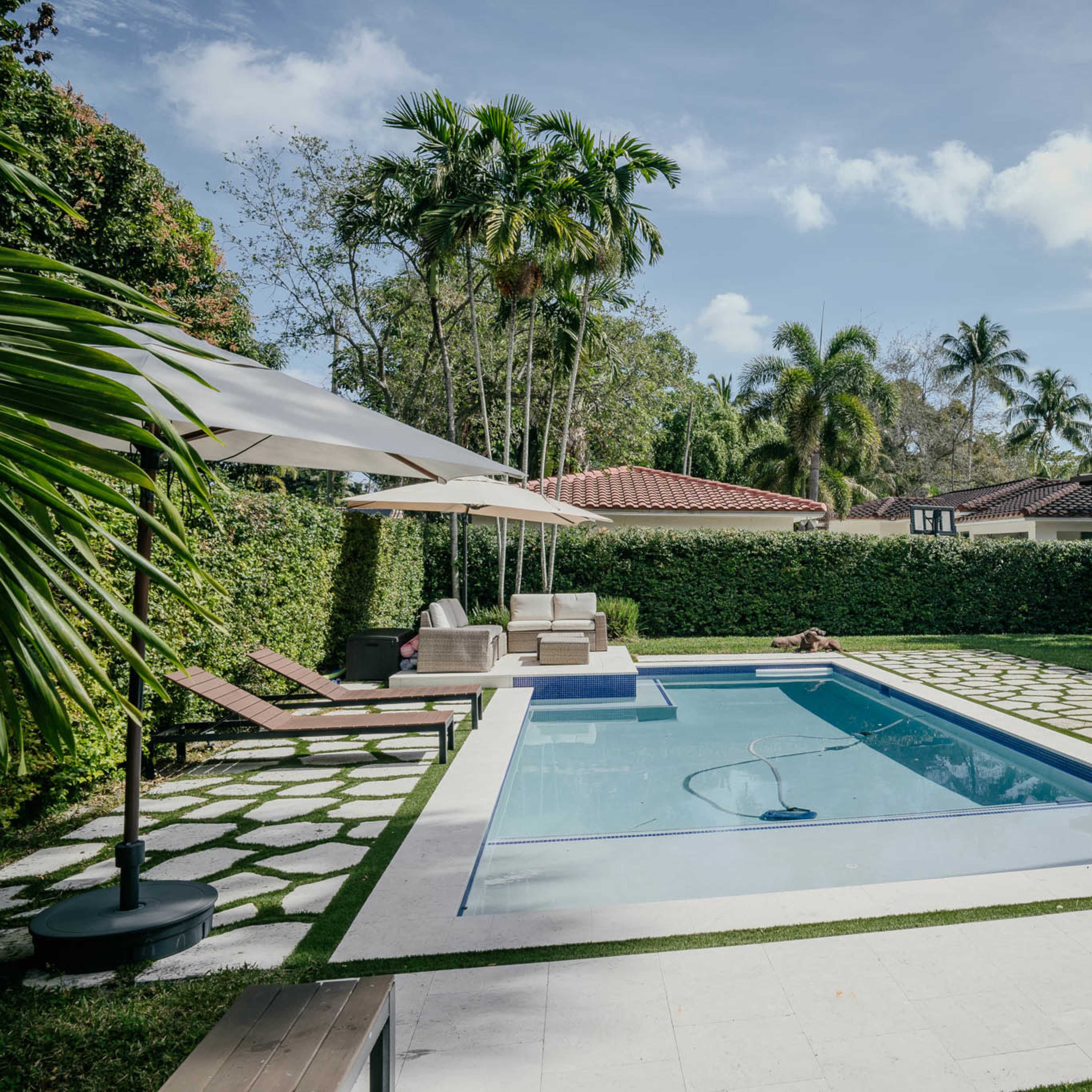 A rectangular swimming pool surrounded by lounge chairs and palm trees in a landscaped backyard.