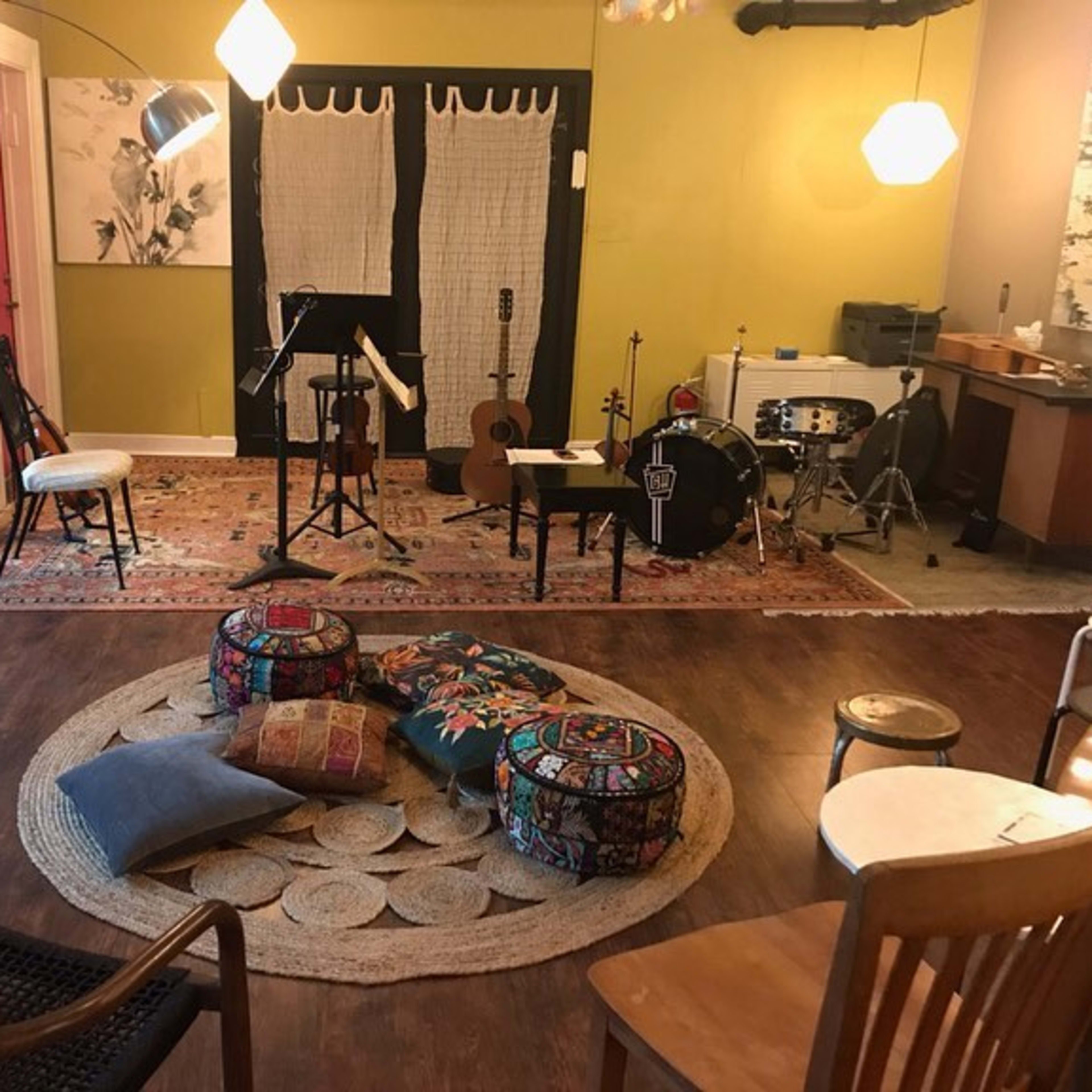 A cozy room set up for music practice, featuring chairs, instruments, and colorful poufs arranged around a circular rug.