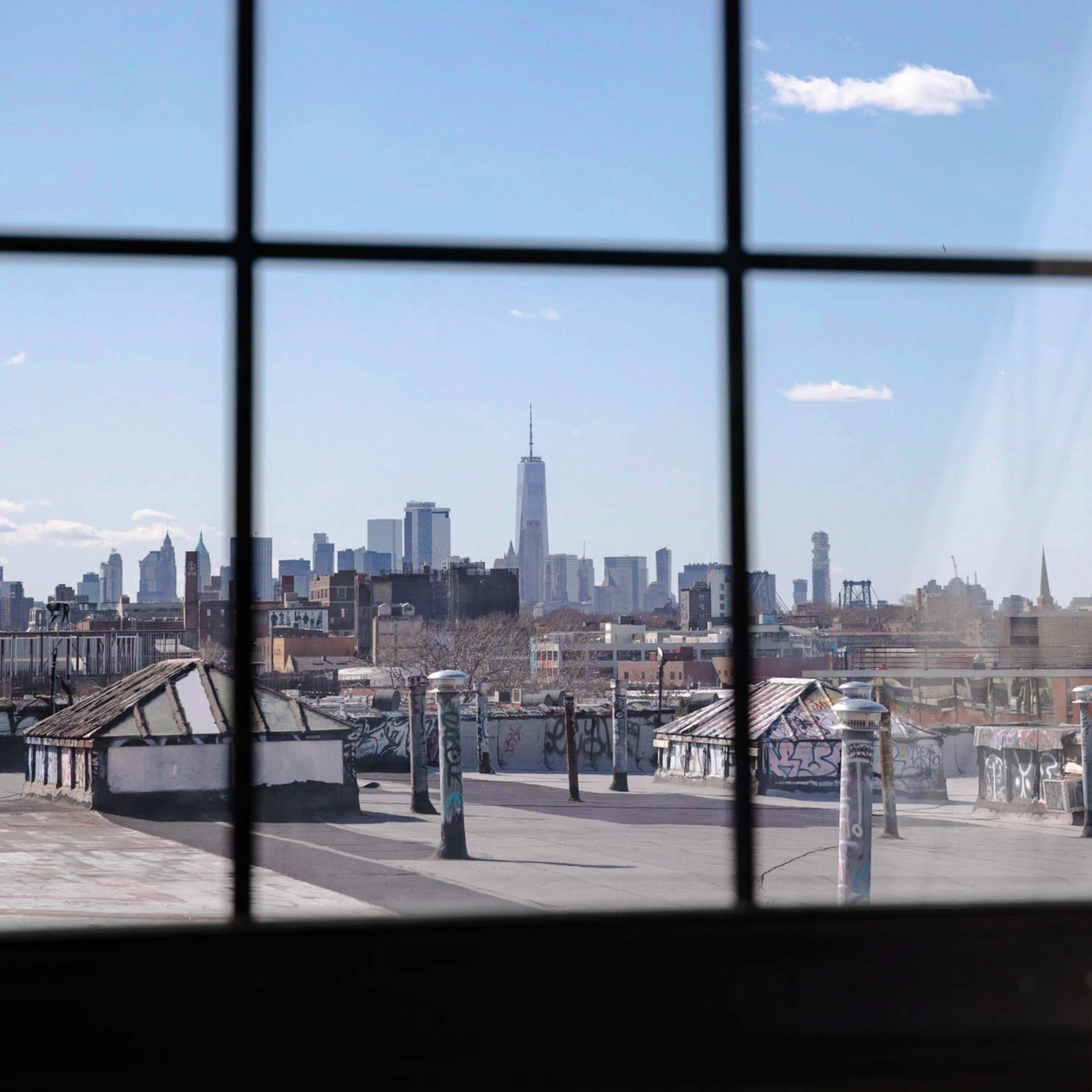 A view of the New York City skyline, featuring the One World Trade Center, is seen through a window with a grid pattern.