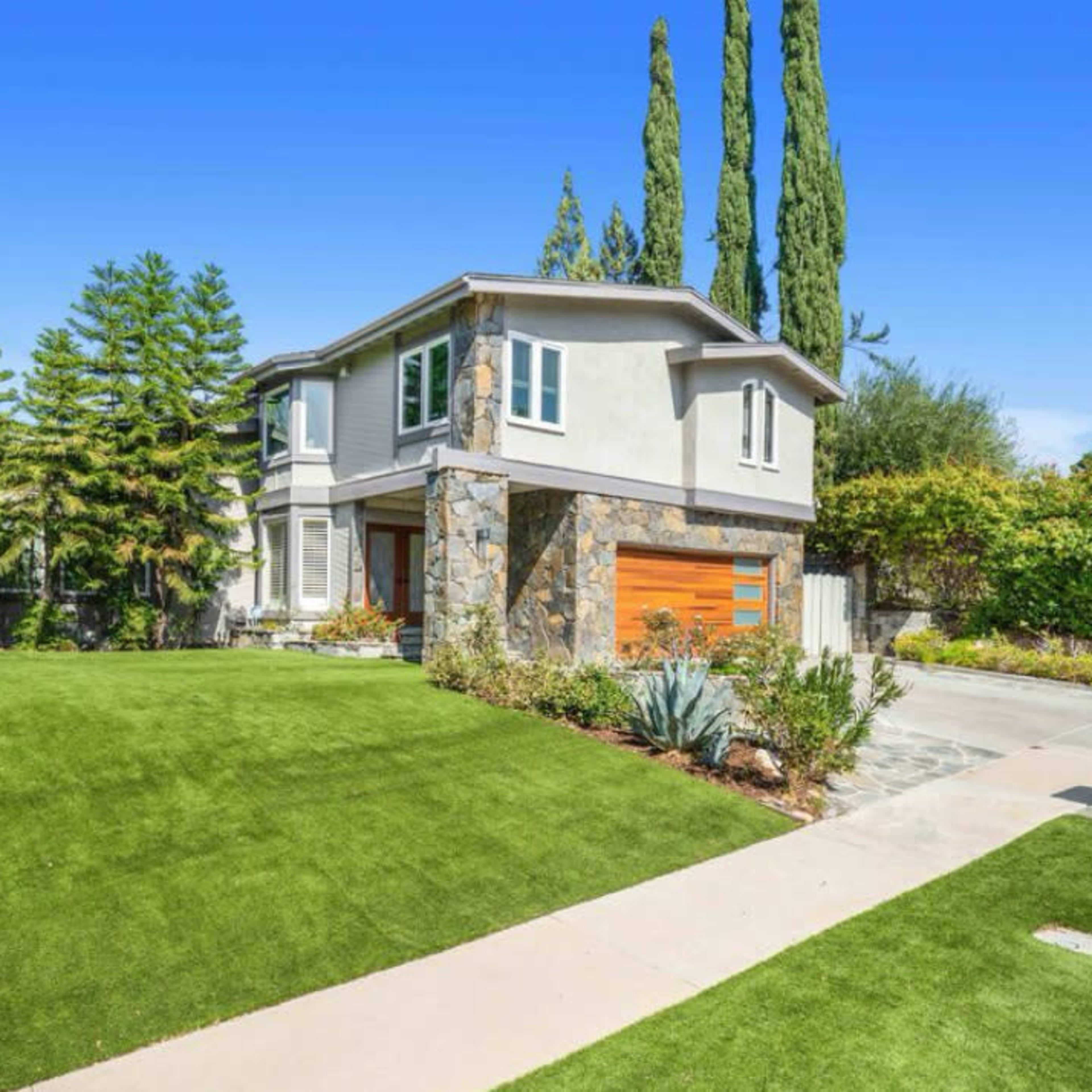 A modern two-story house features a landscaped front yard with artificial green grass and stone accents.