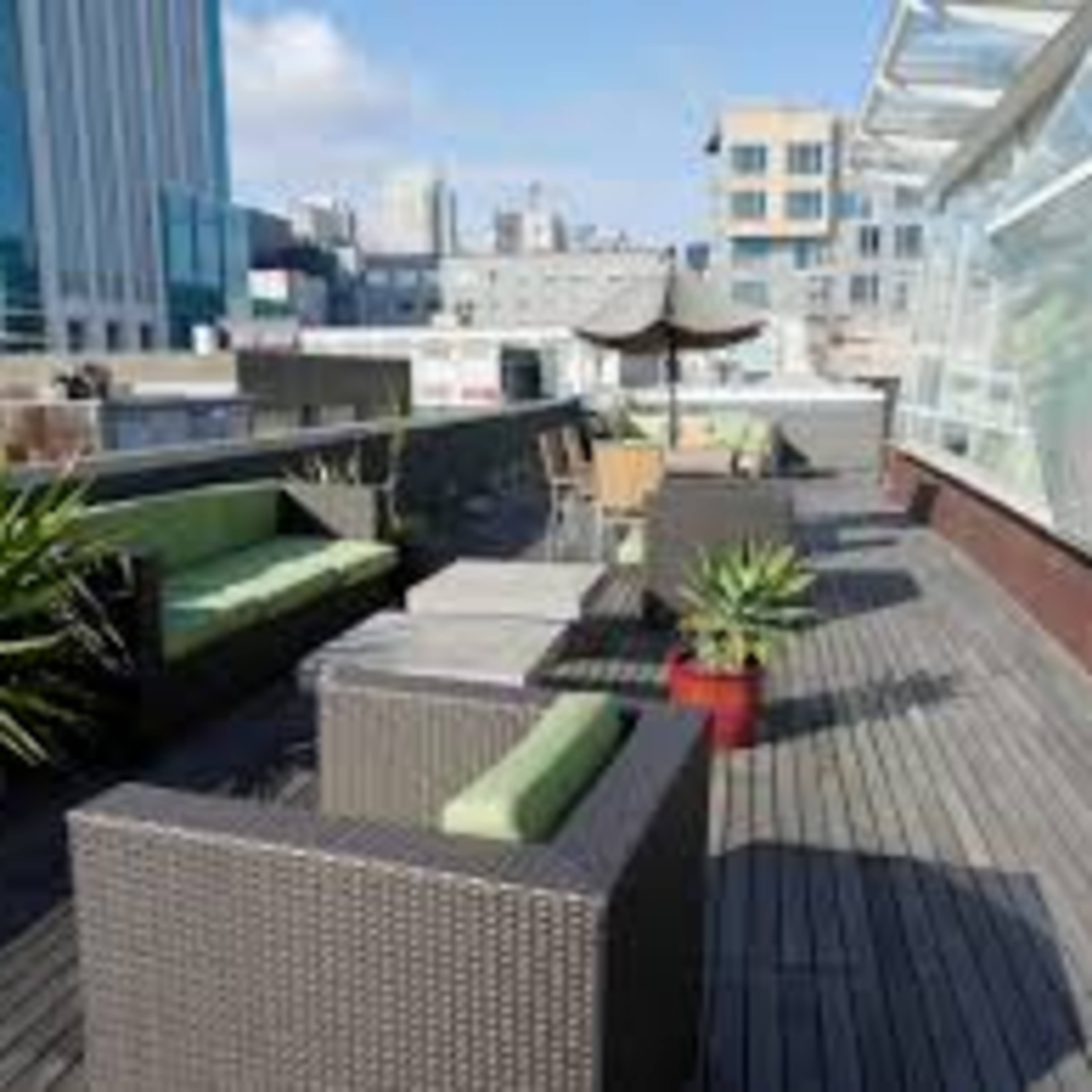 A modern rooftop terrace with seating, small plants, and a city skyline in the background.
