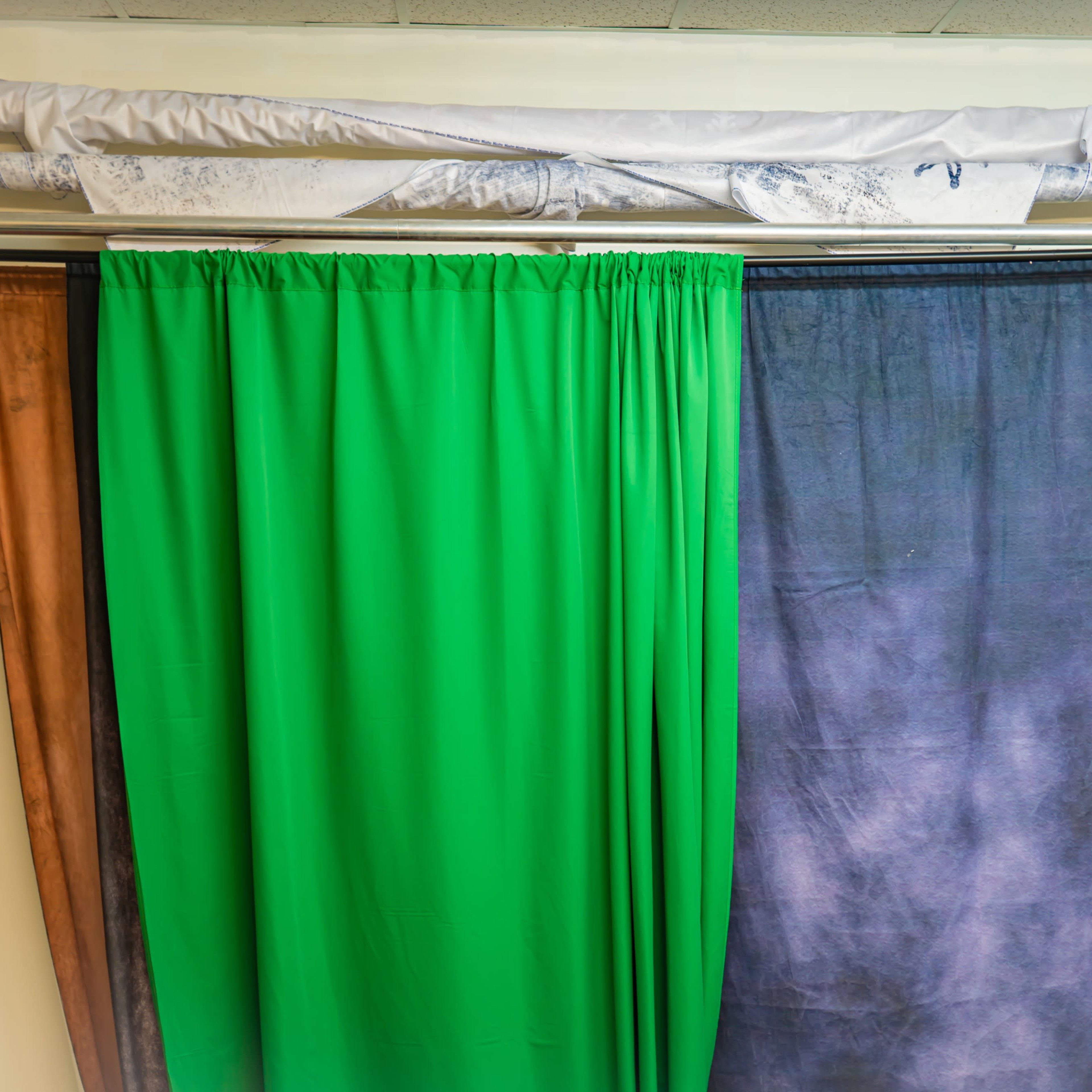 A set of fabric curtains in various colors hanging from a rack against a wall.