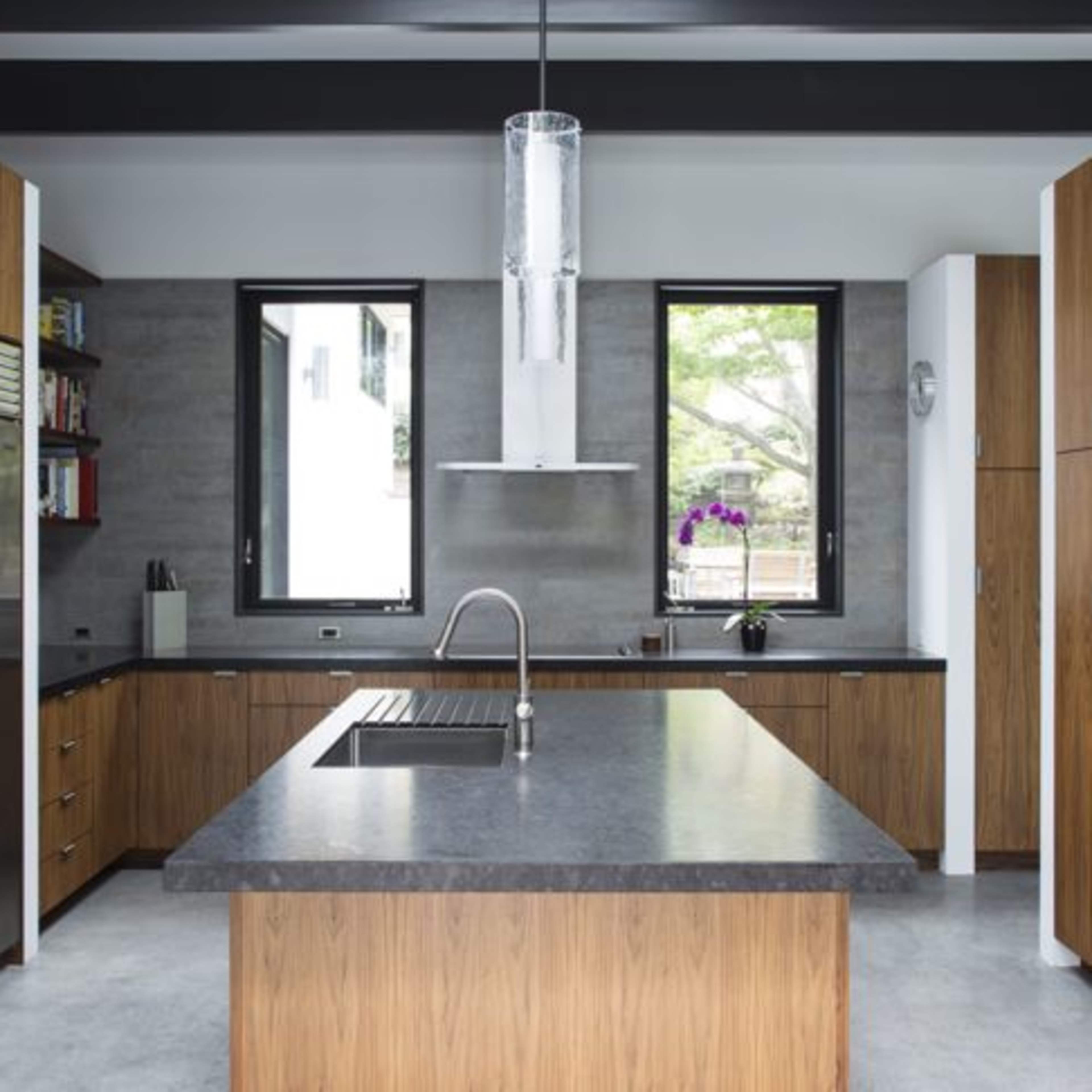 A modern kitchen with wooden cabinetry, a large central island, and stainless steel appliances, illuminated by a pendant light.