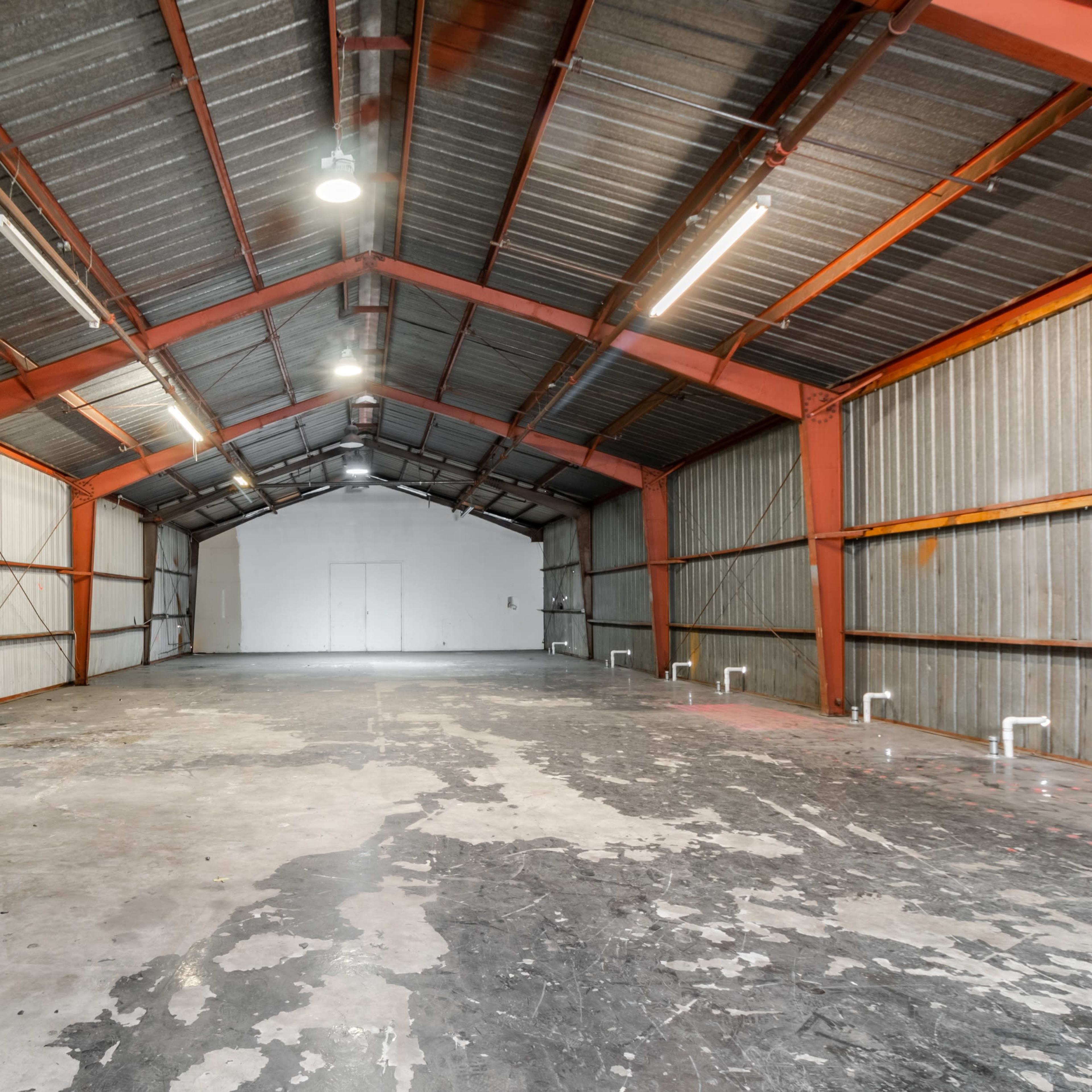 The interior of a large, empty warehouse with a high ceiling, metal beams, and concrete flooring.