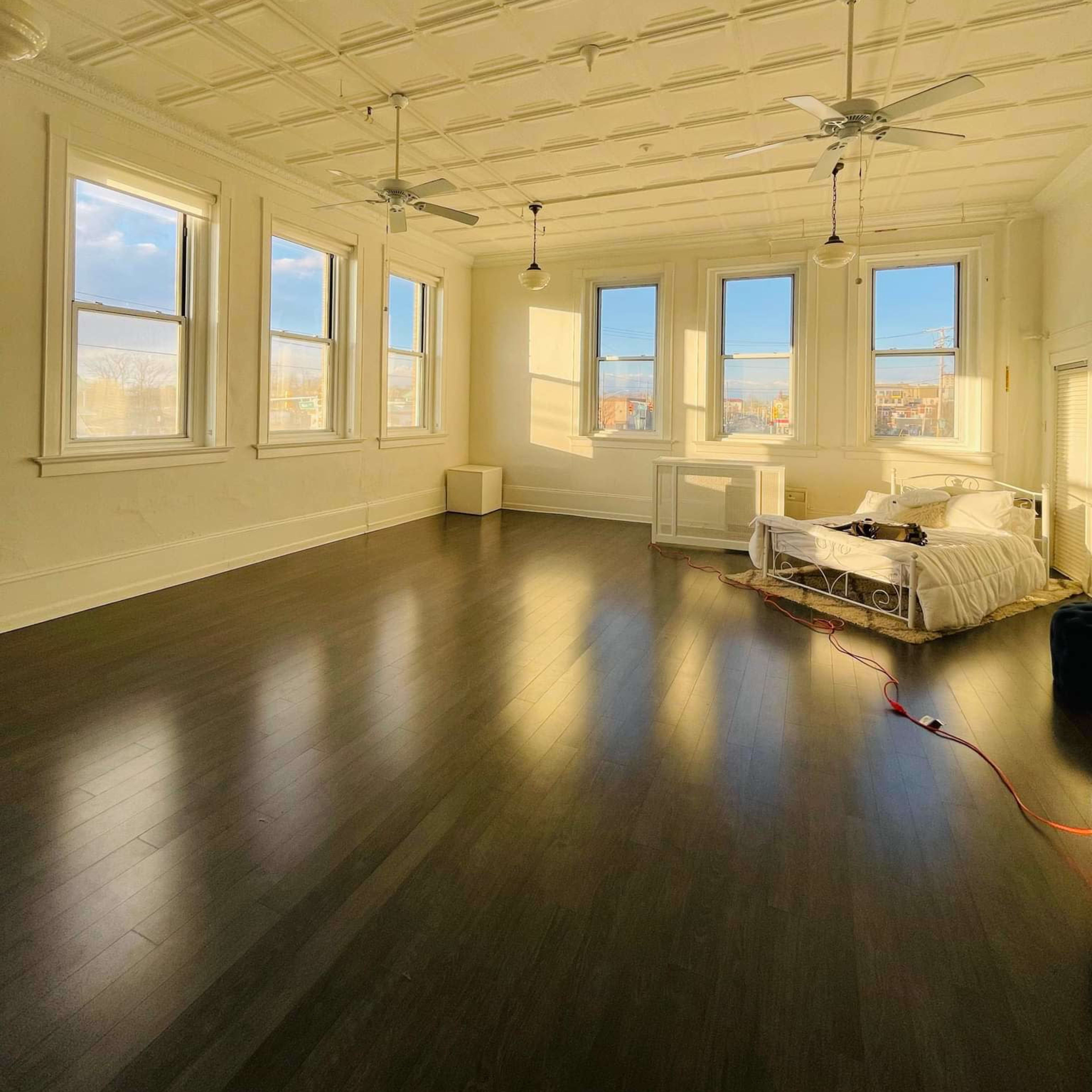 A spacious, well-lit bedroom with large windows, a bed, and wooden flooring.