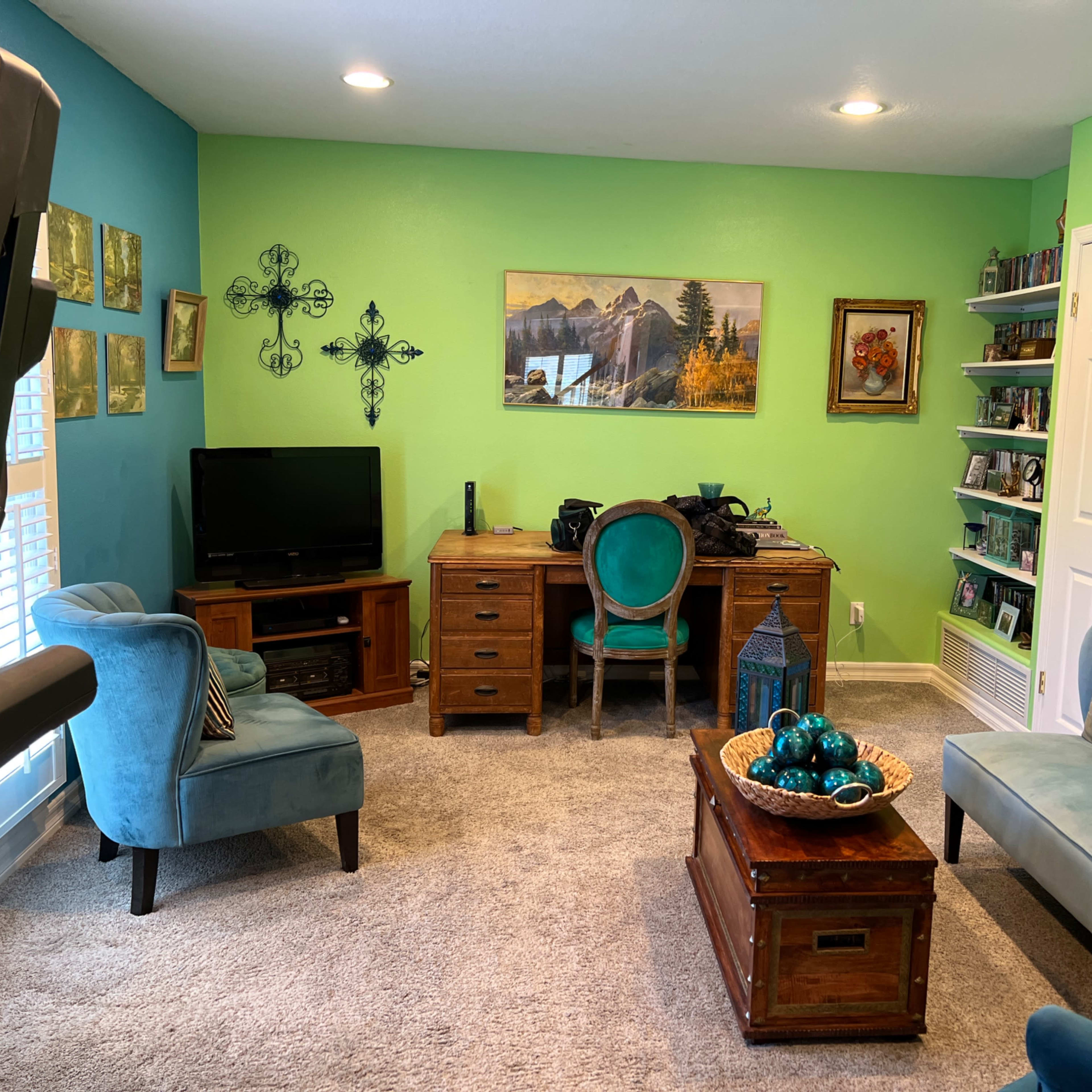 The room features a green and blue color scheme with a desk, chairs, a television, and various decorations on the walls and shelves.