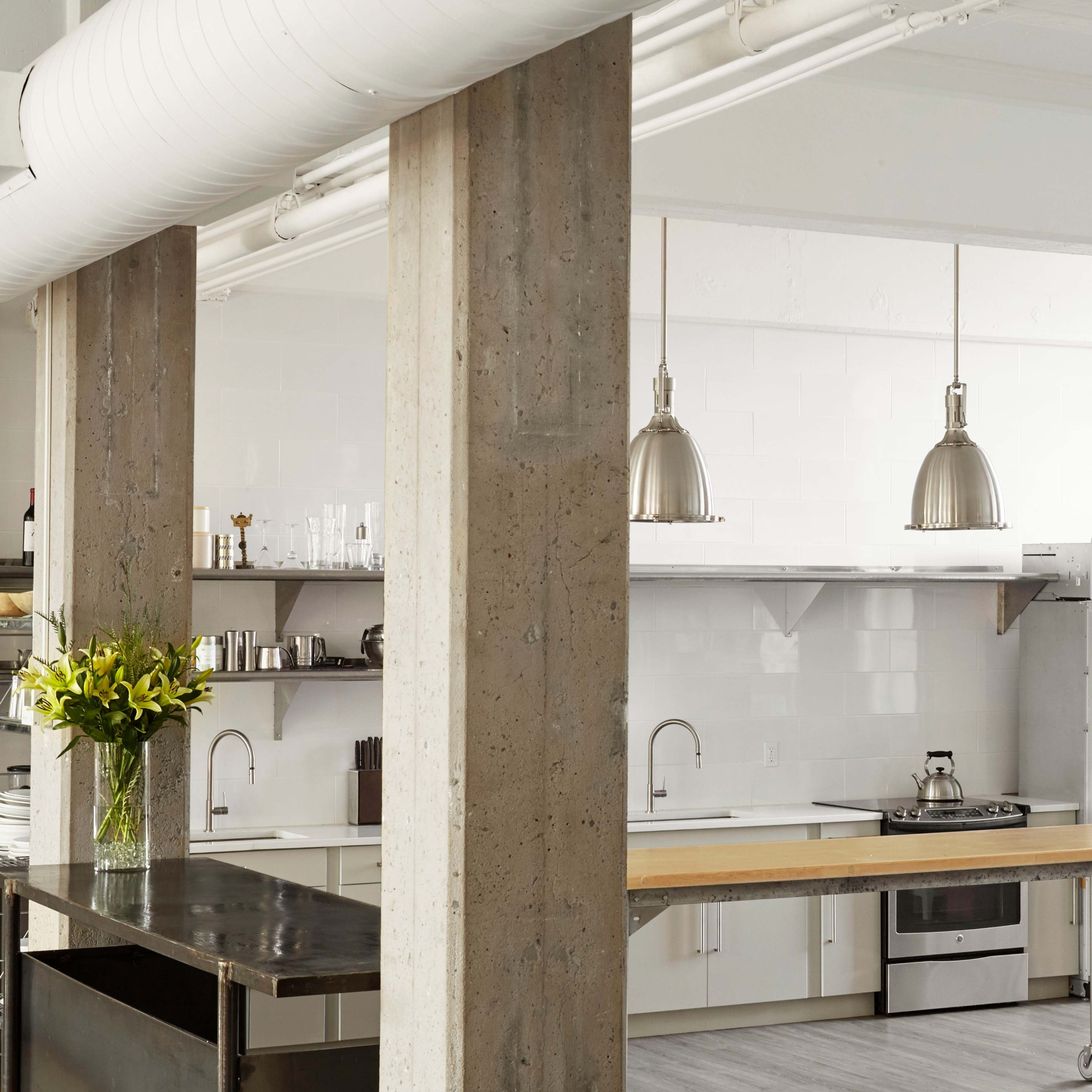 A modern kitchen with stainless steel appliances, a central wooden island, and concrete structural columns.
