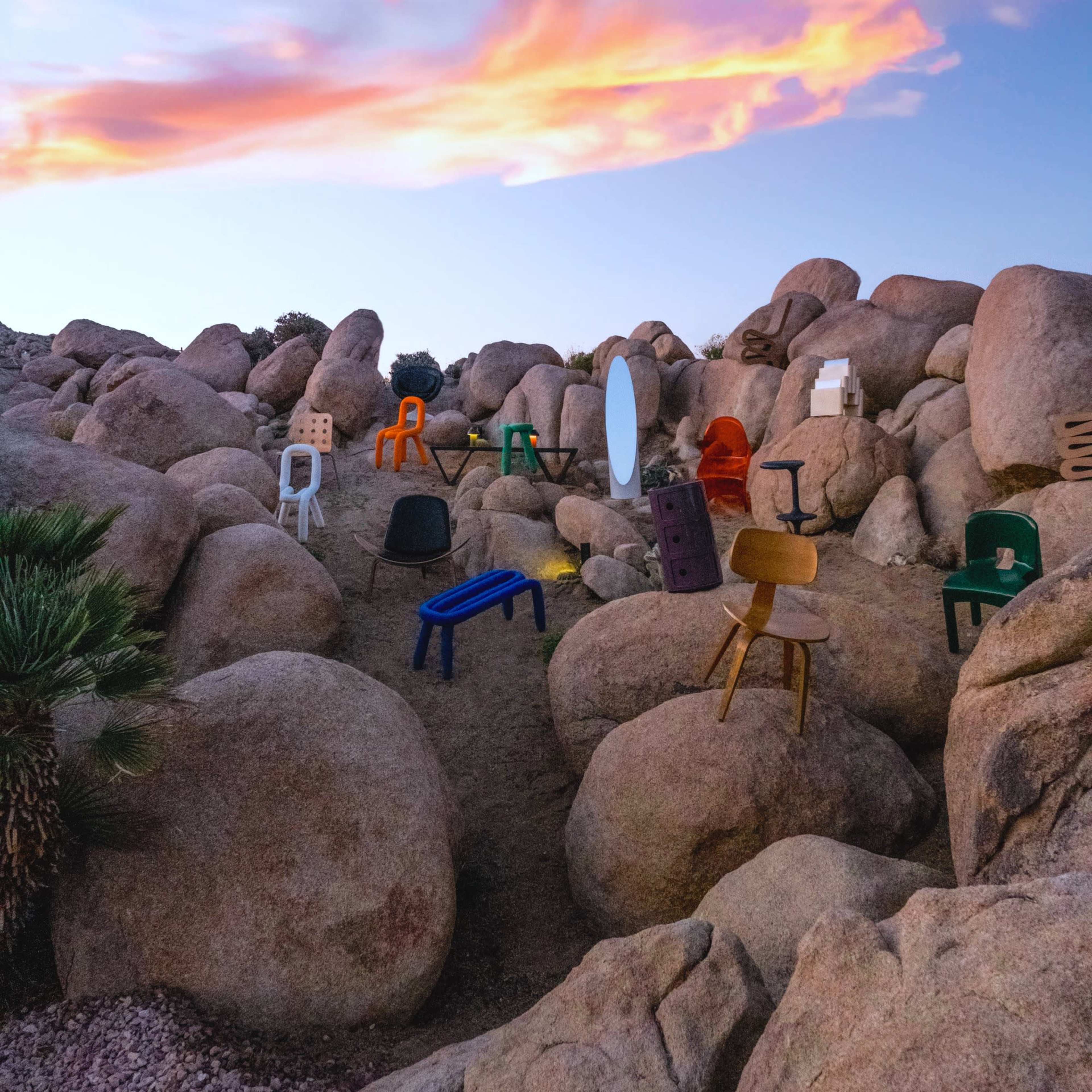 The scene features various colorful chairs arranged among large boulders under a vibrant sky at dusk.