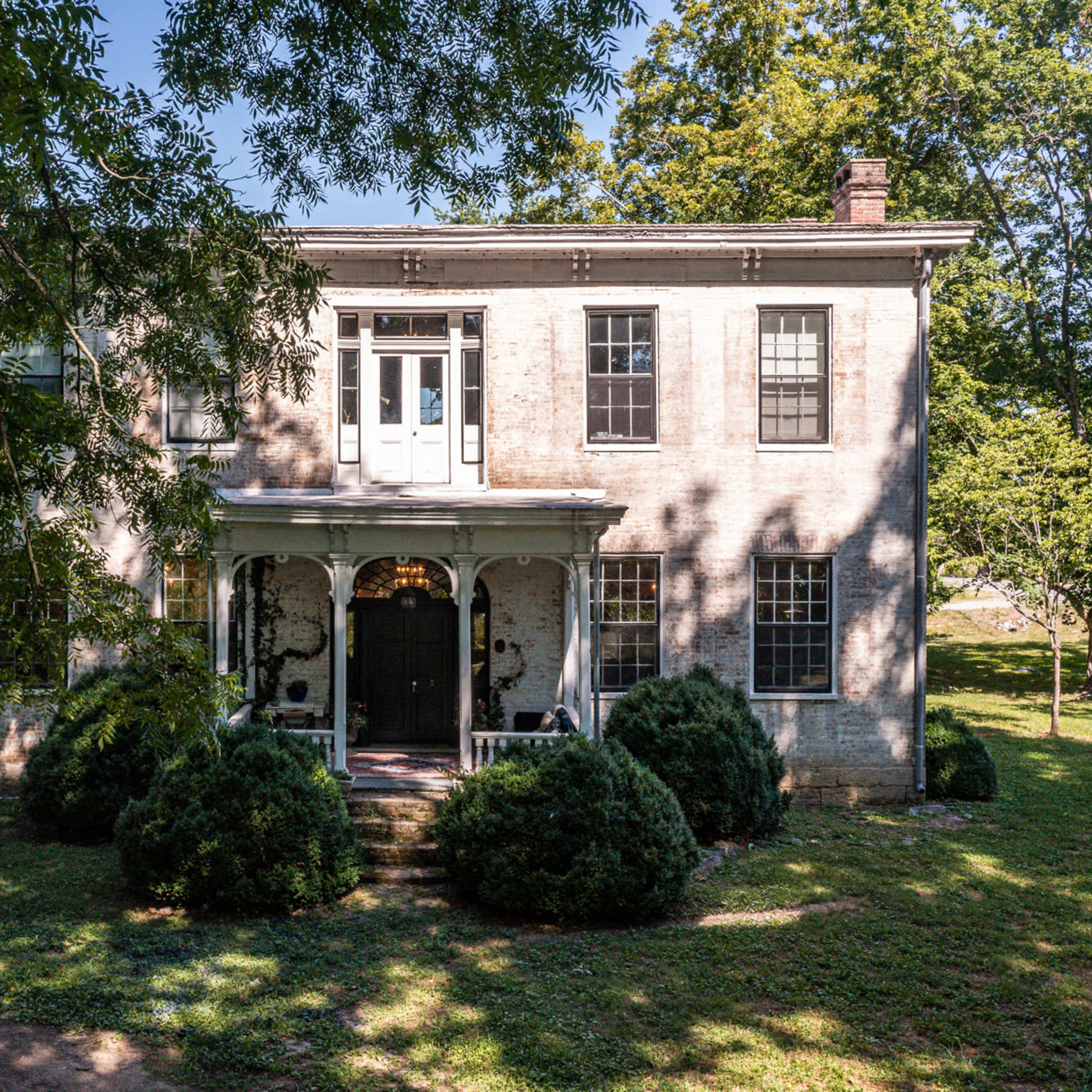 A two-story, rectangular brick house with a central entrance and surrounded by manicured shrubs on a grassy lawn.