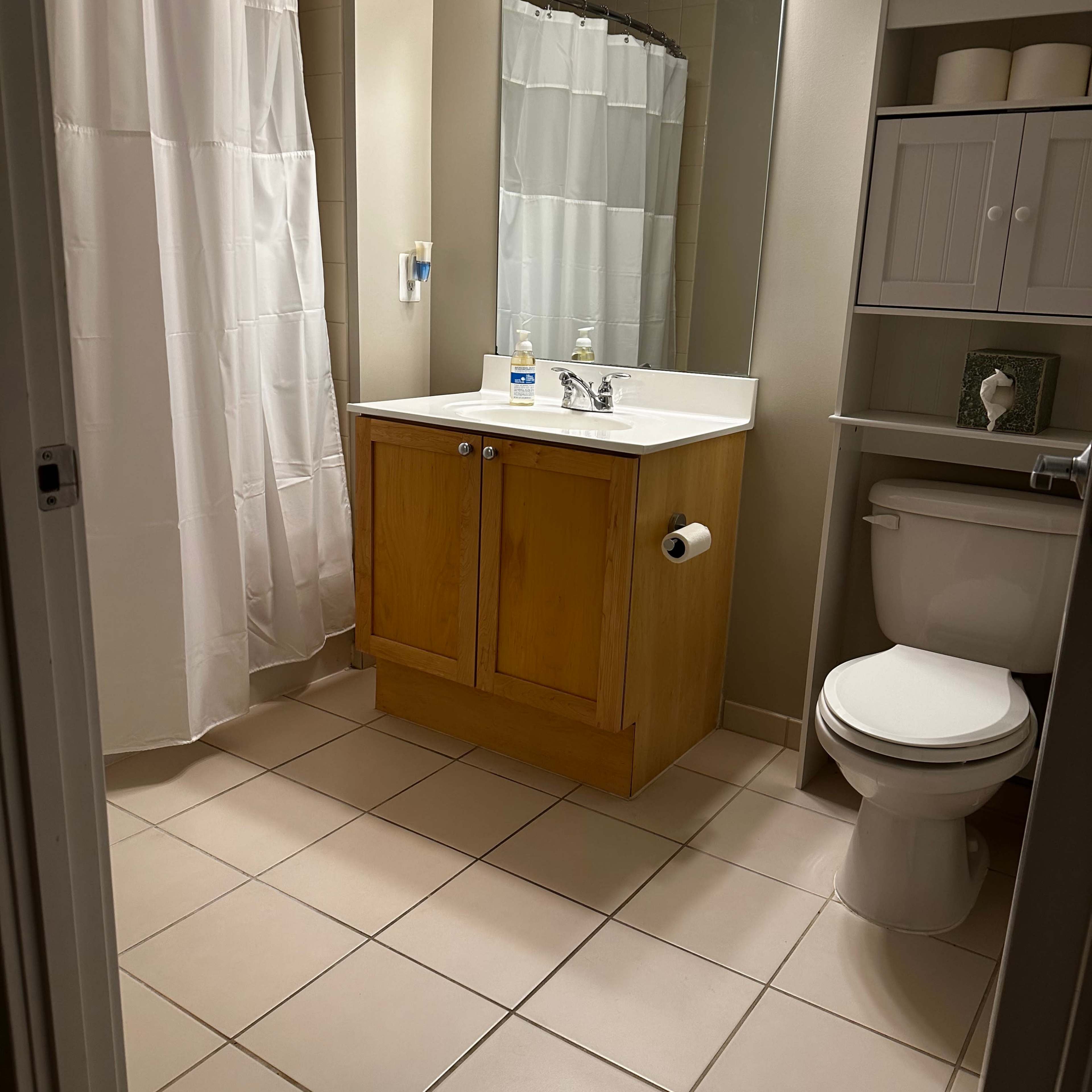 A bathroom with a shower curtain, sink with a wooden cabinet, a toilet, and a mirror above the sink.
