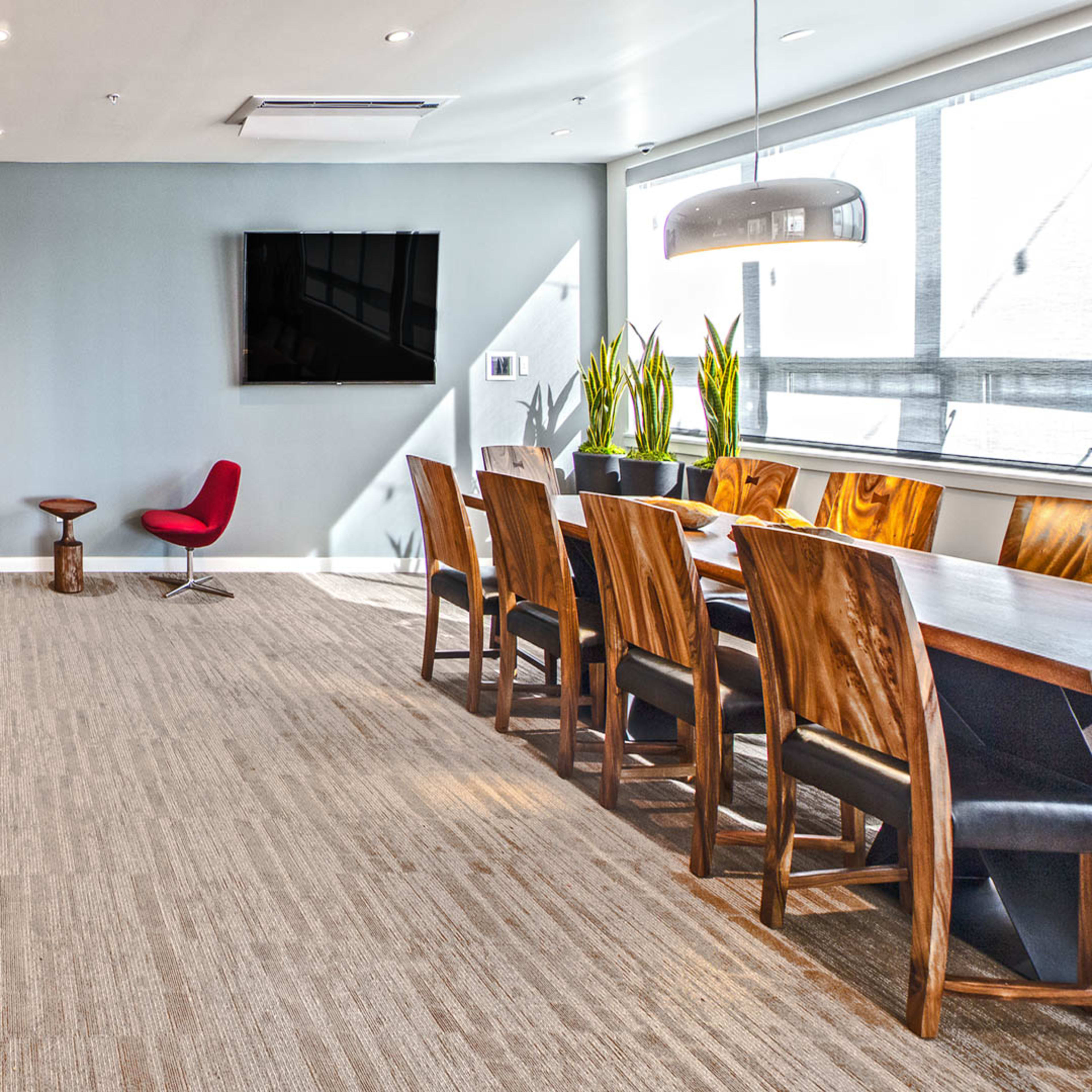 A modern kitchen and dining area features a large island with bar seating, wooden dining chairs around a long table, and a wall-mounted television.
