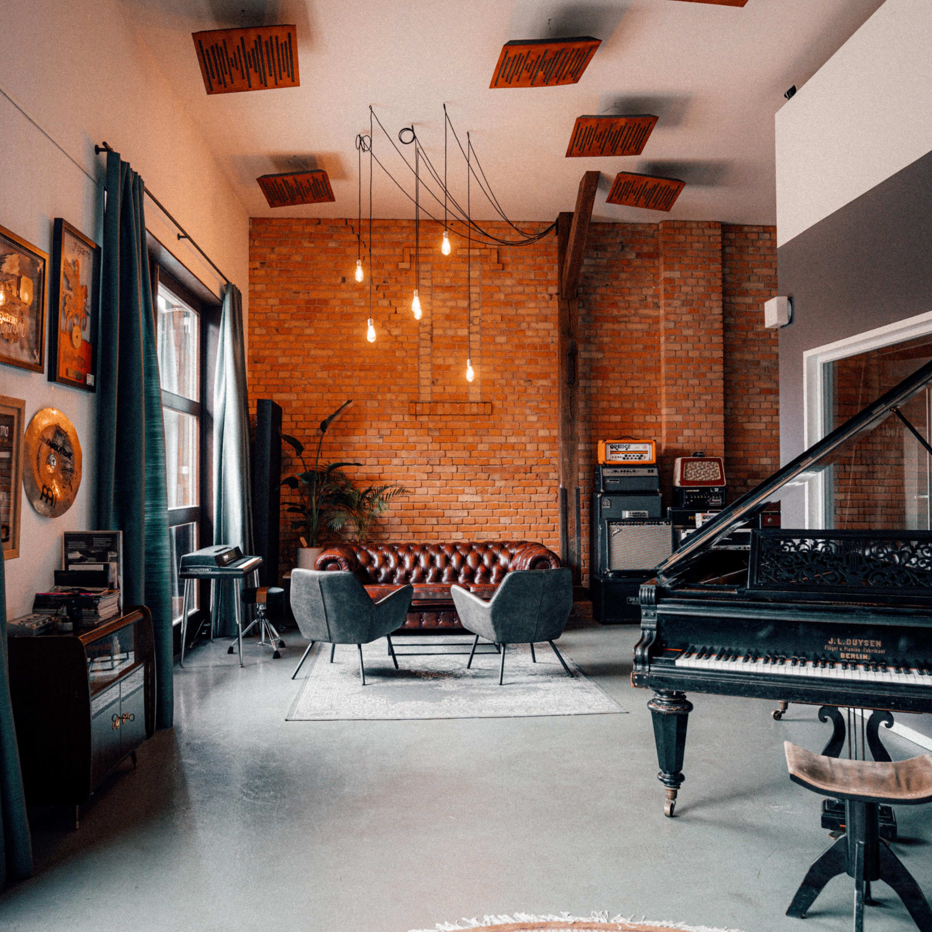 A stylish lounge area featuring a grand piano, comfortable seating, and exposed brick walls, illuminated by hanging pendant lights.