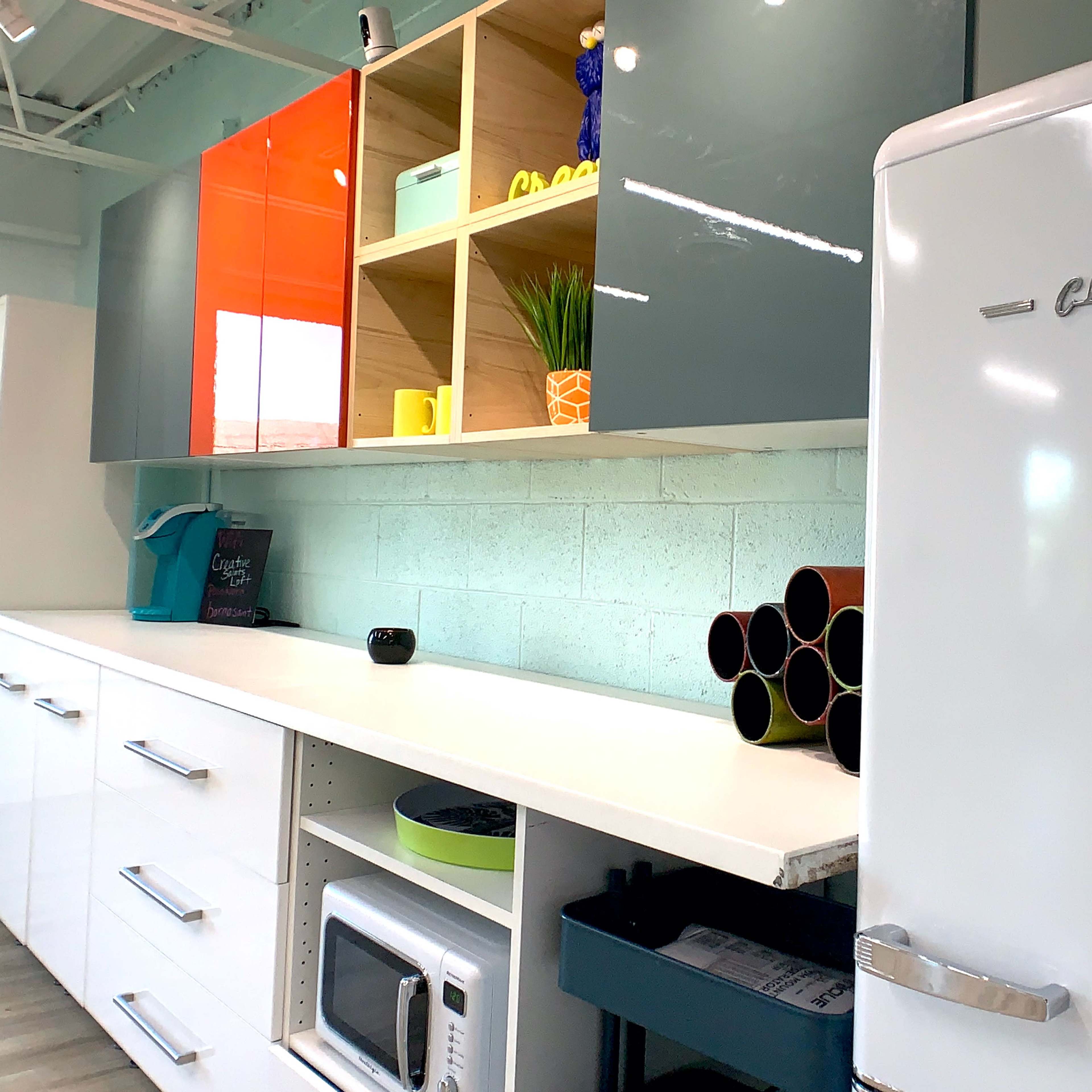A modern kitchen interior with a white refrigerator, a microwave, and shelves displaying colorful items against a light-blue wall.