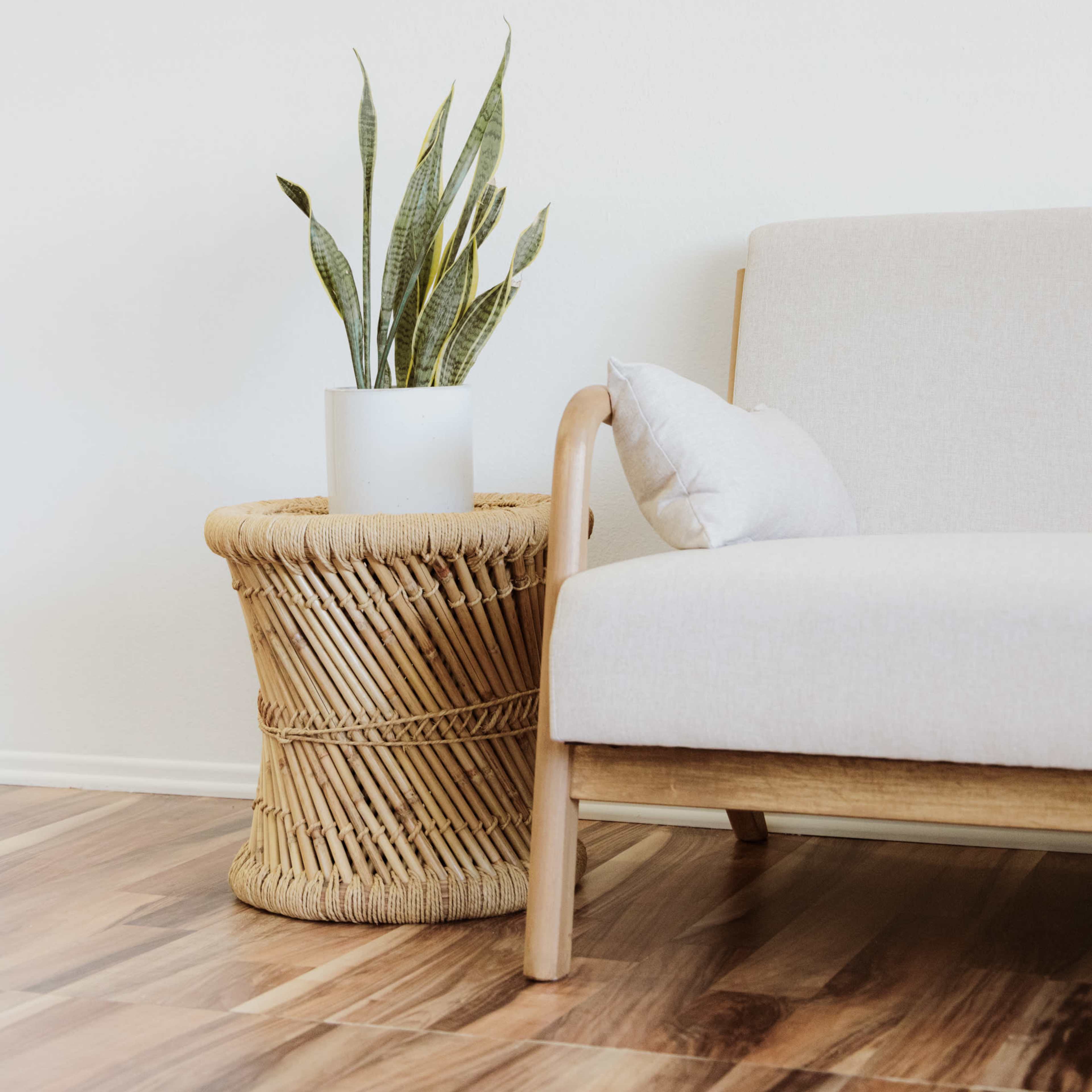 A light-colored sofa sits beside a woven basket table topped with a potted plant in a minimalist room.