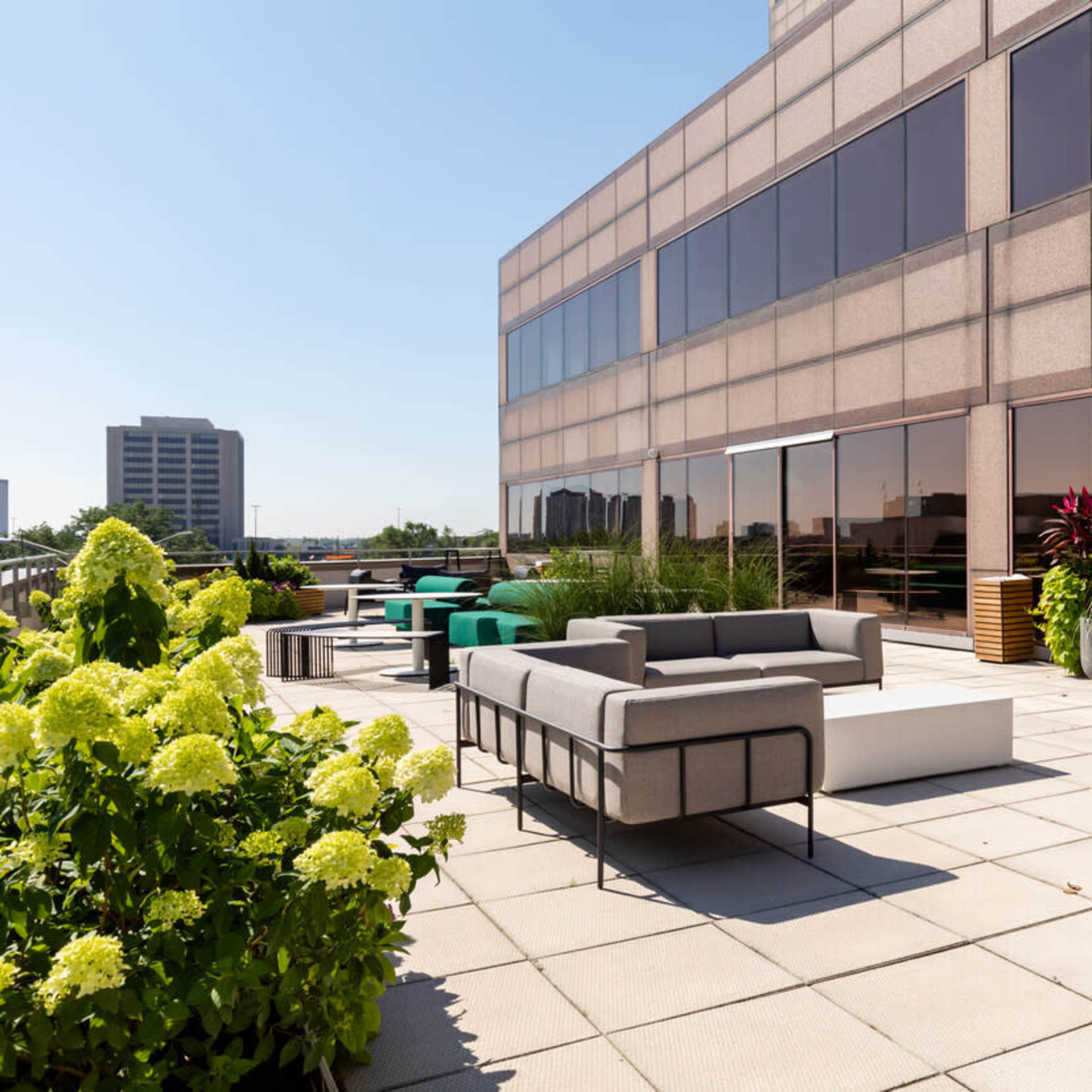 A spacious rooftop terrace featuring modern seating areas, potted plants, and a clear blue sky in the background.
