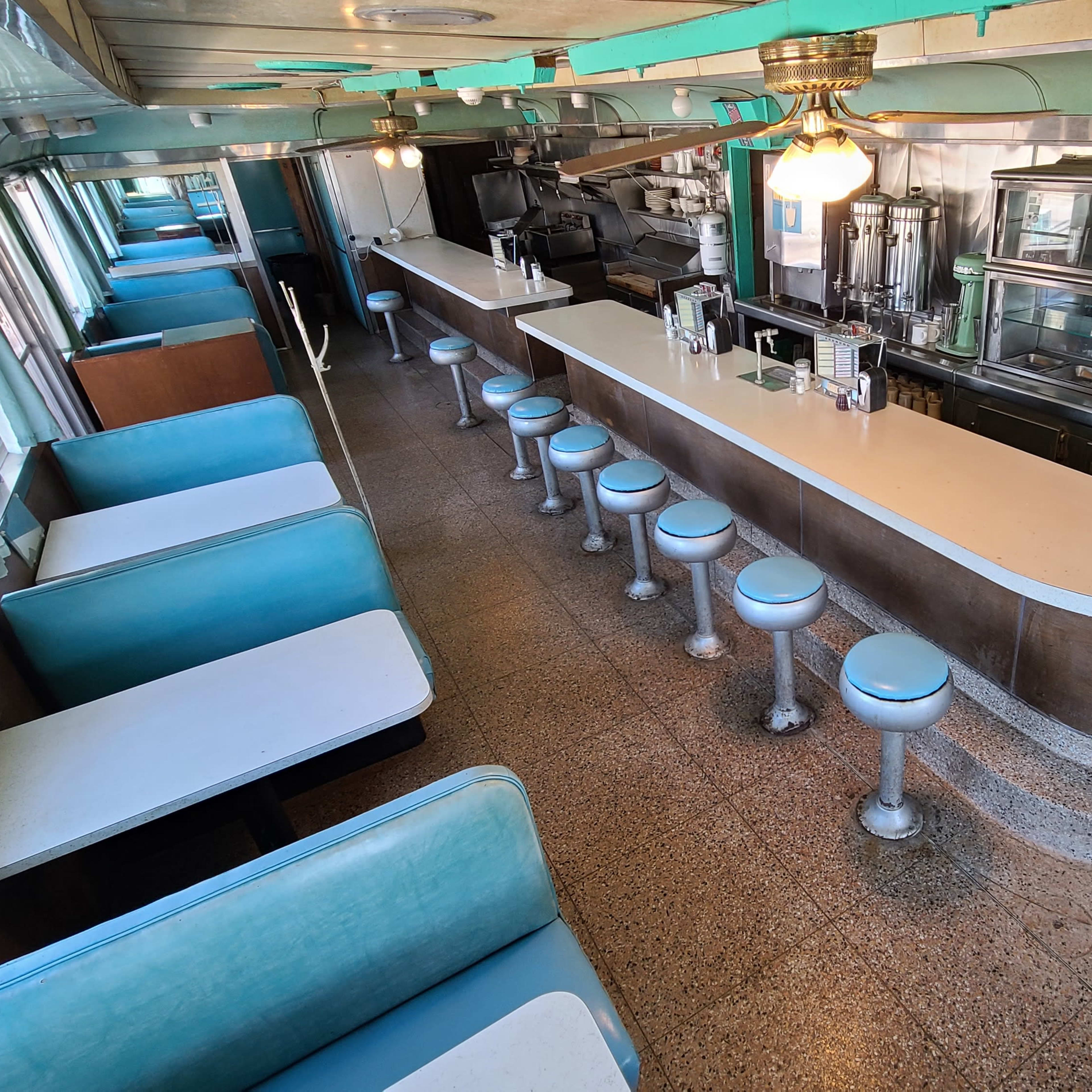 The interior of a vintage diner featuring a long counter with stools and turquoise seating booths.