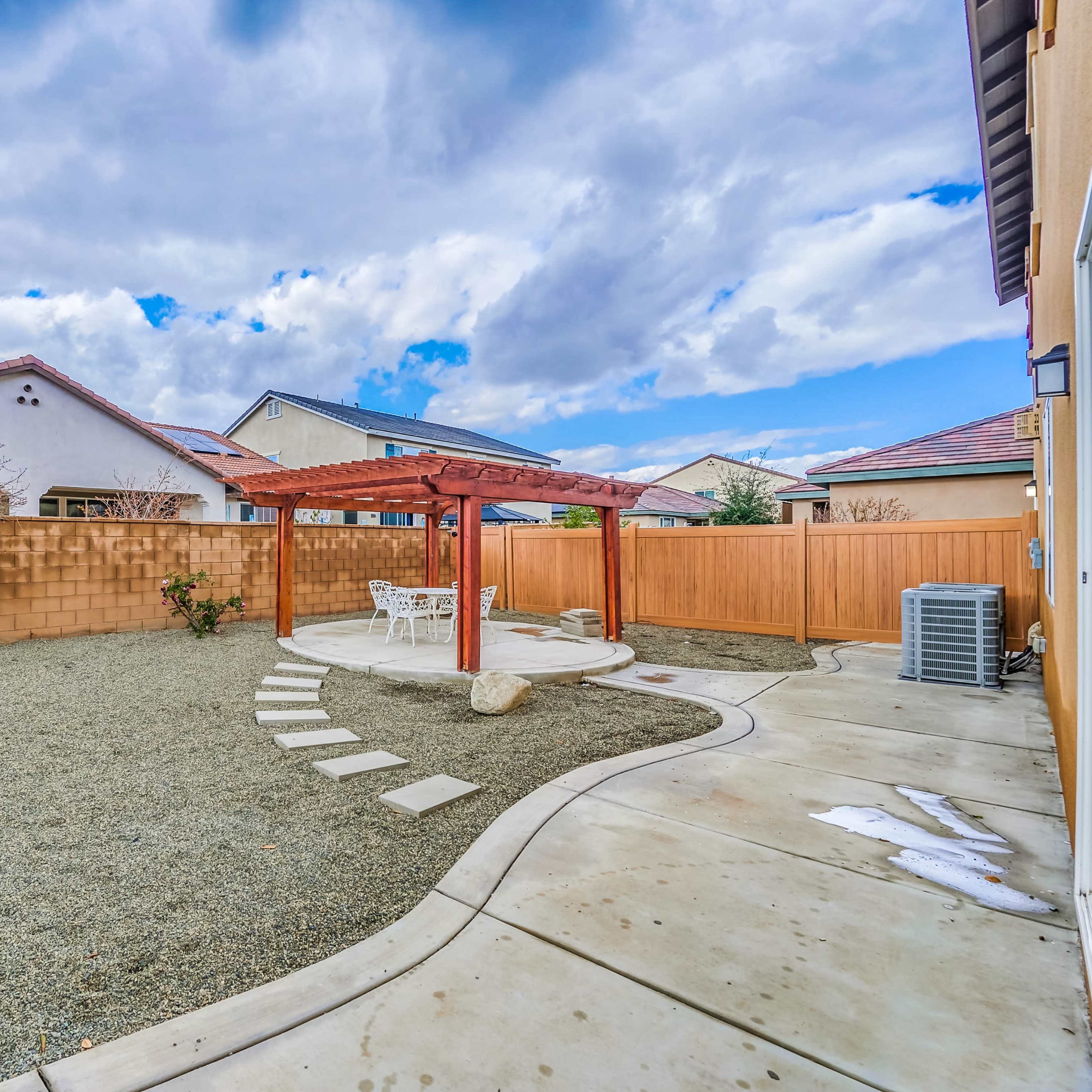A backyard with a gravel area, a pergola, stepping stones, and a wooden fence enclosing the space.
