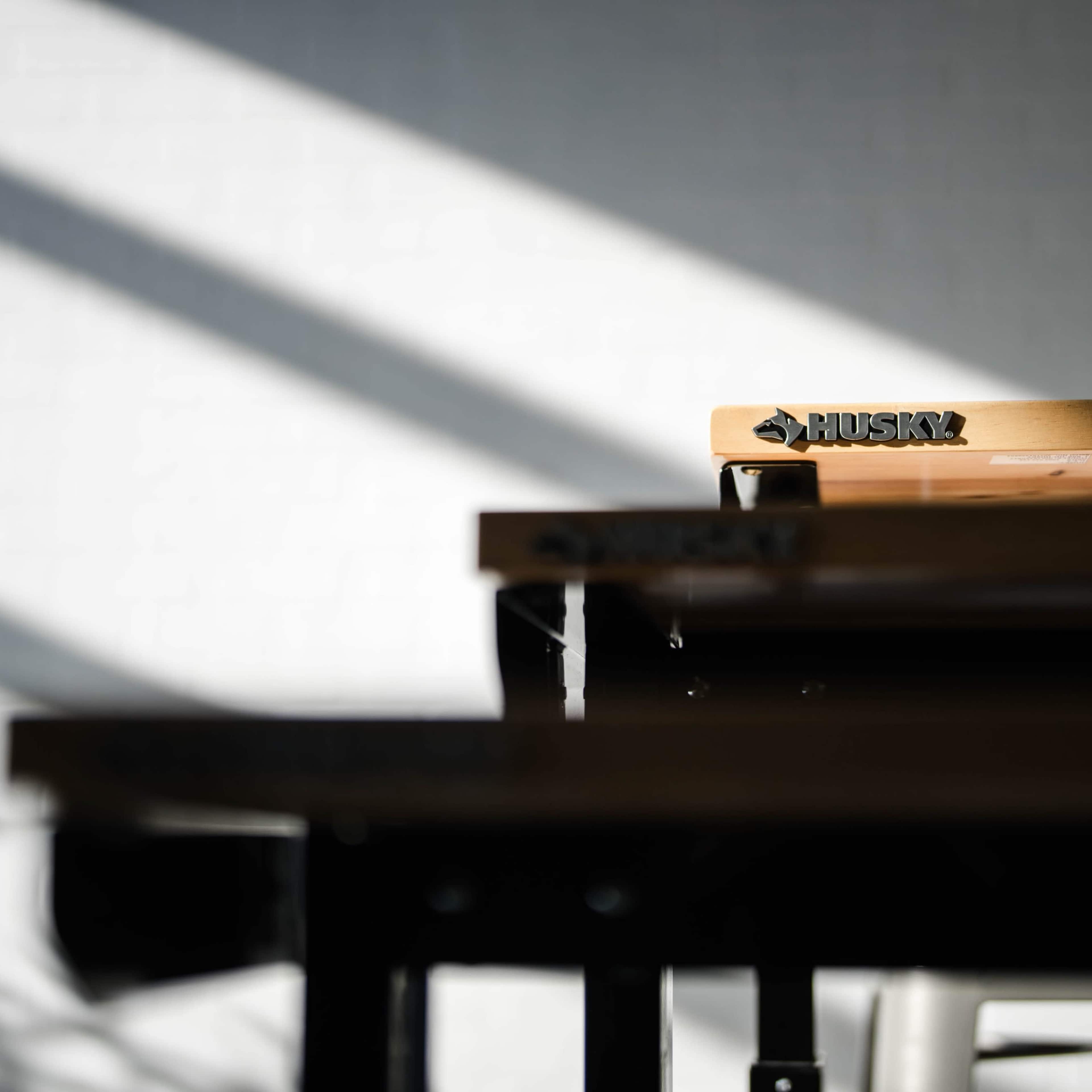 A row of wooden workbenches with a focus on a branded bench in bright sunlight casting shadows on a white wall.