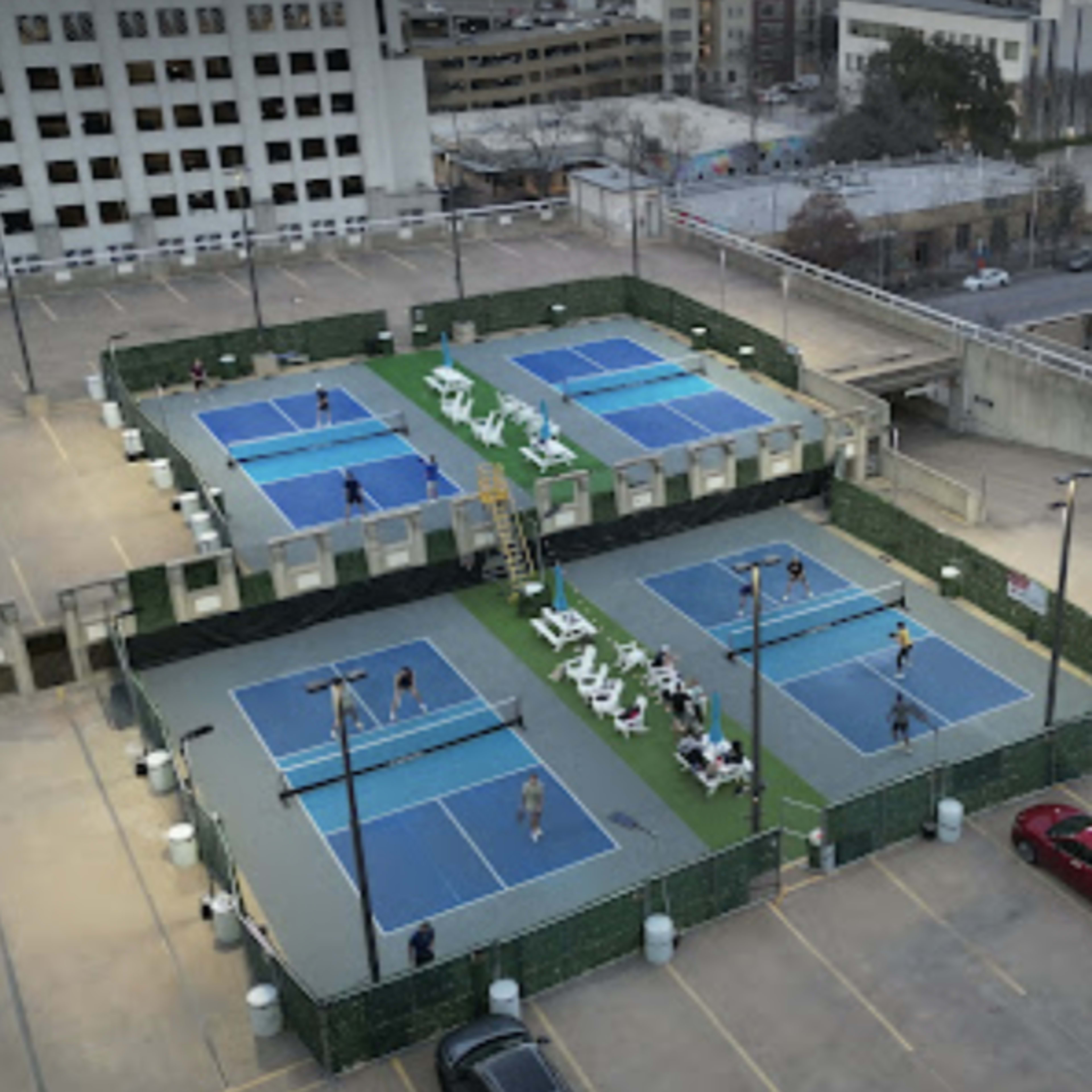 An elevated view of a rooftop tennis facility with multiple courts surrounded by green fencing and players actively participating in games.