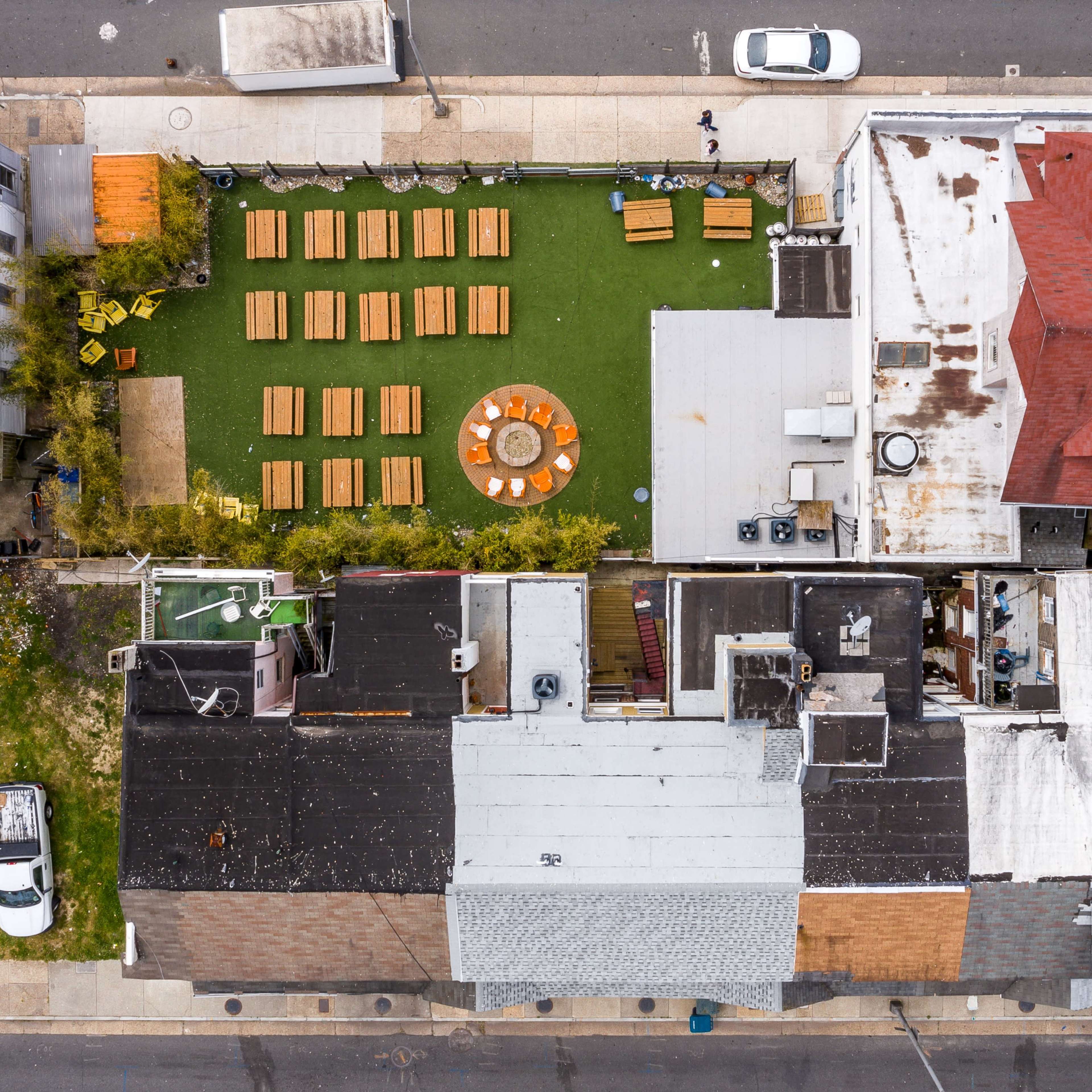 An aerial view of a neighborhood featuring several buildings surrounding a green space with seating arrangements and a central fire pit.