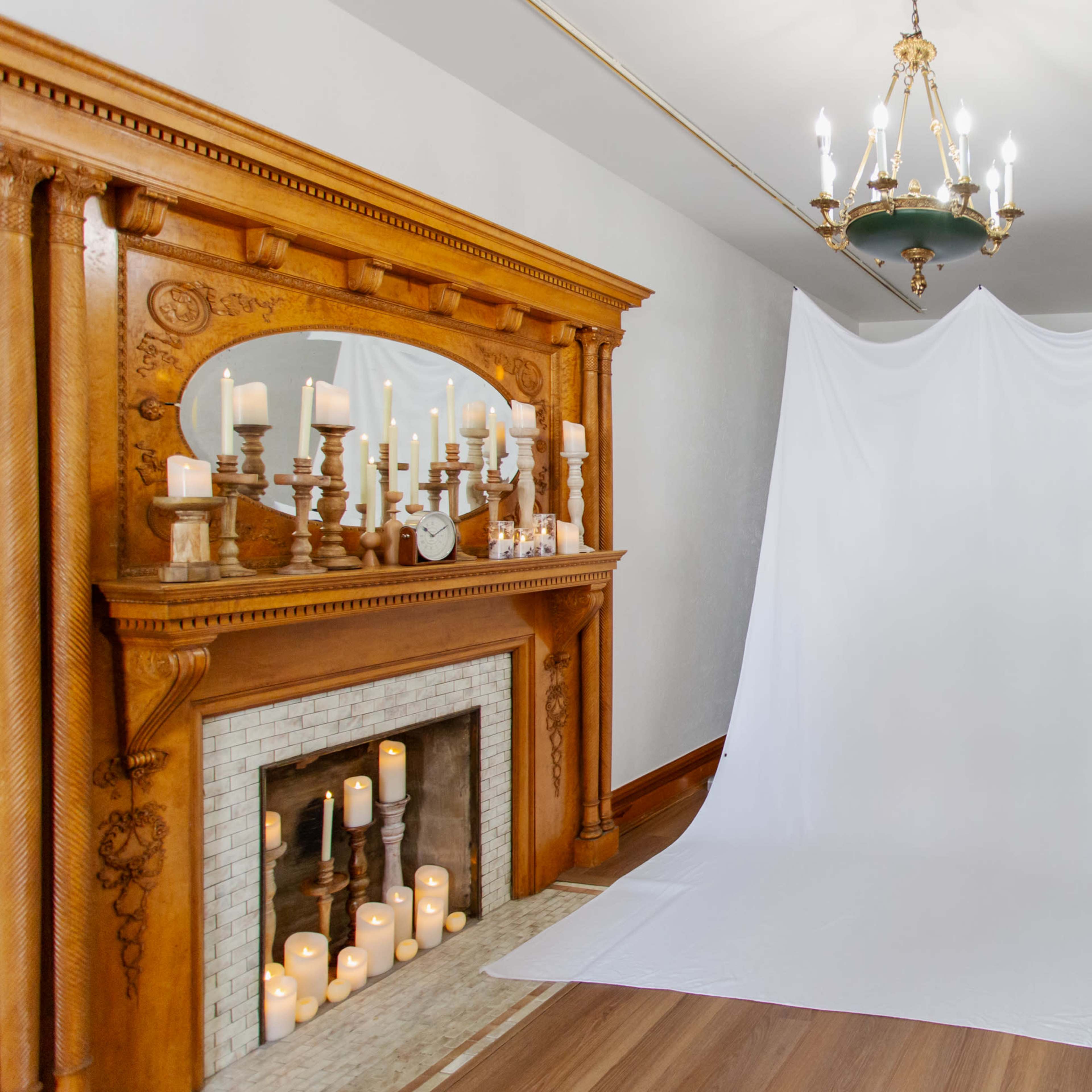 A large white backdrop stands in front of a wooden fireplace adorned with candles in a well-lit room.