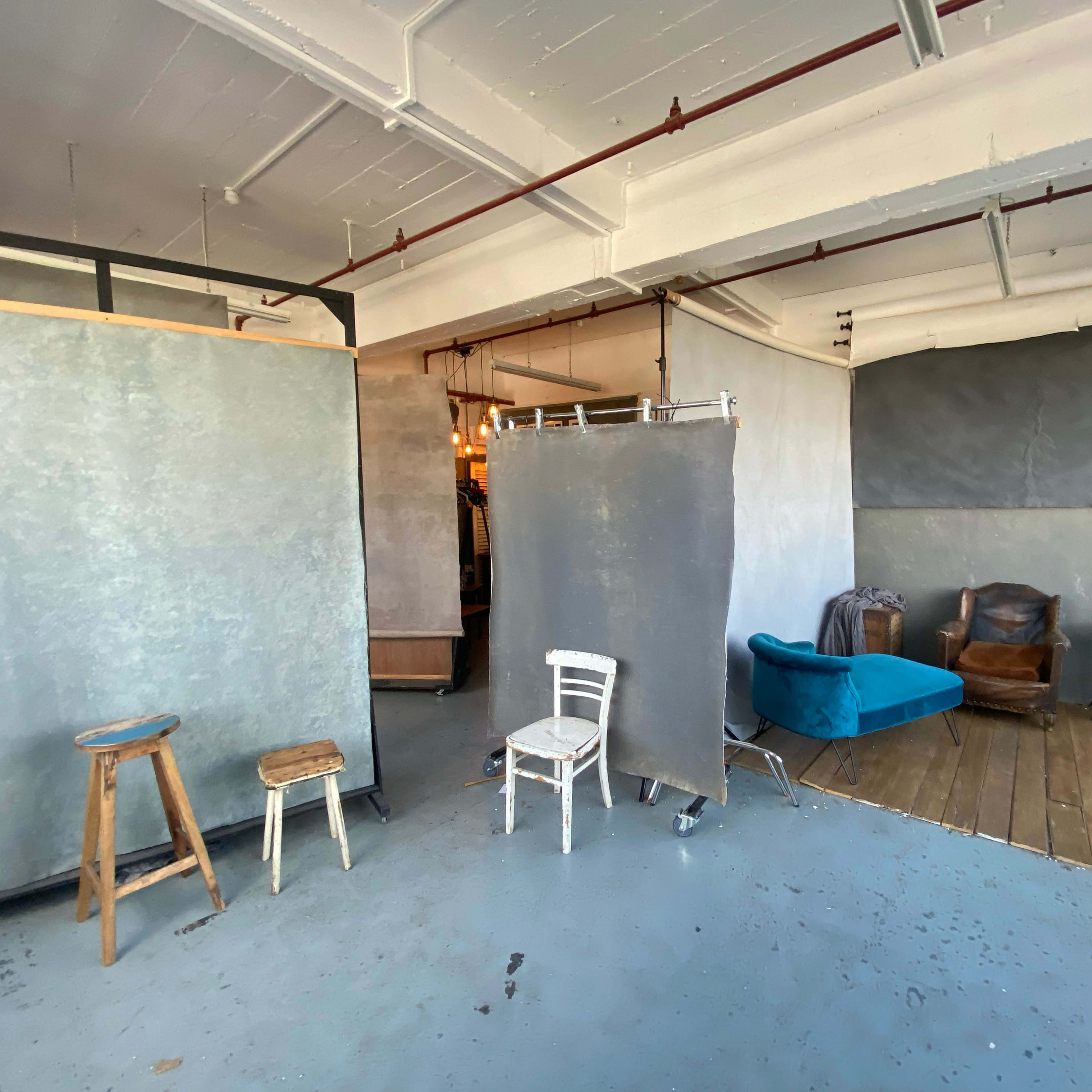 A spacious room with gray backdrops, wooden floors, and a mix of furniture including chairs and a couch.