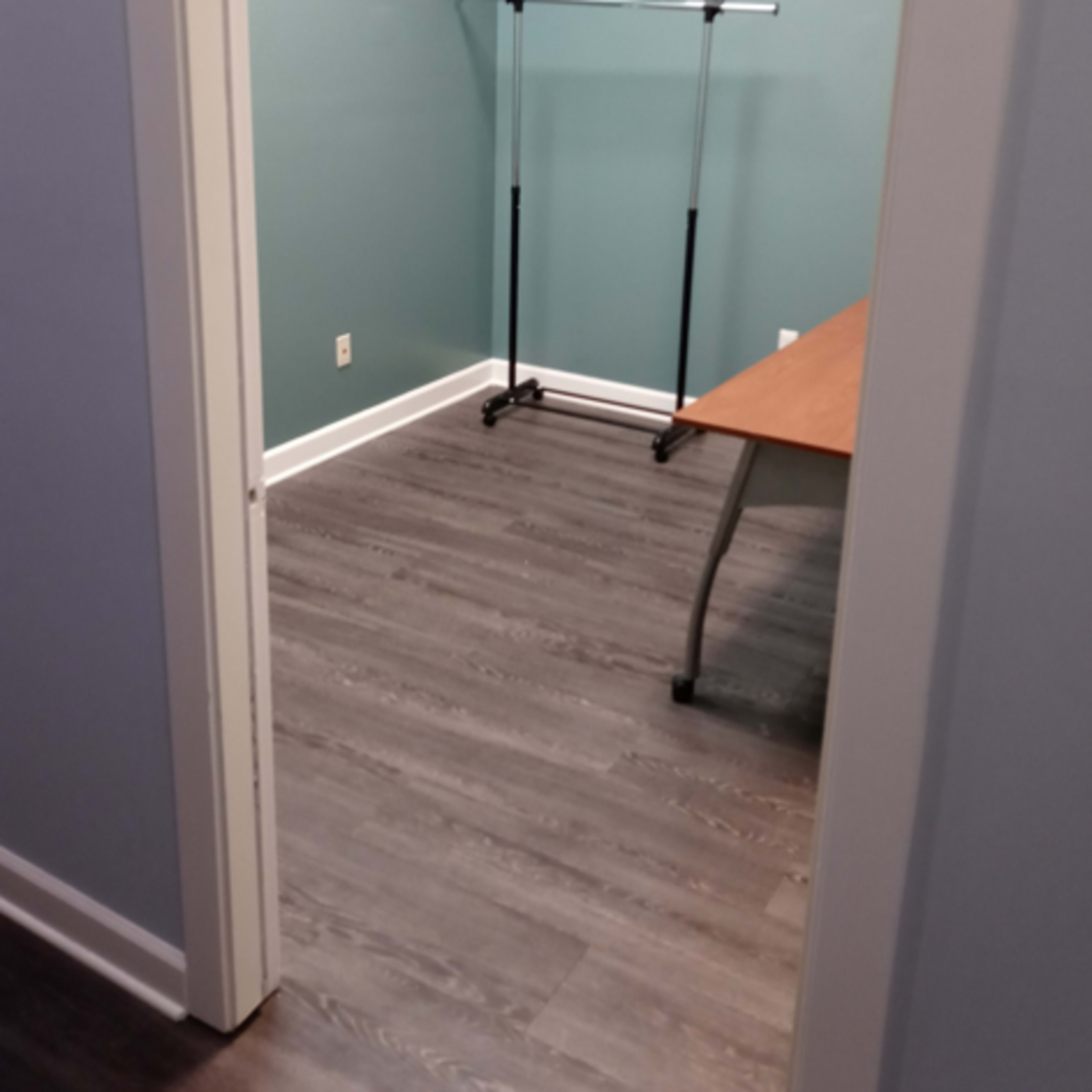 A small room with a clothes rack and a desk against the wall, featuring teal walls and wooden flooring.