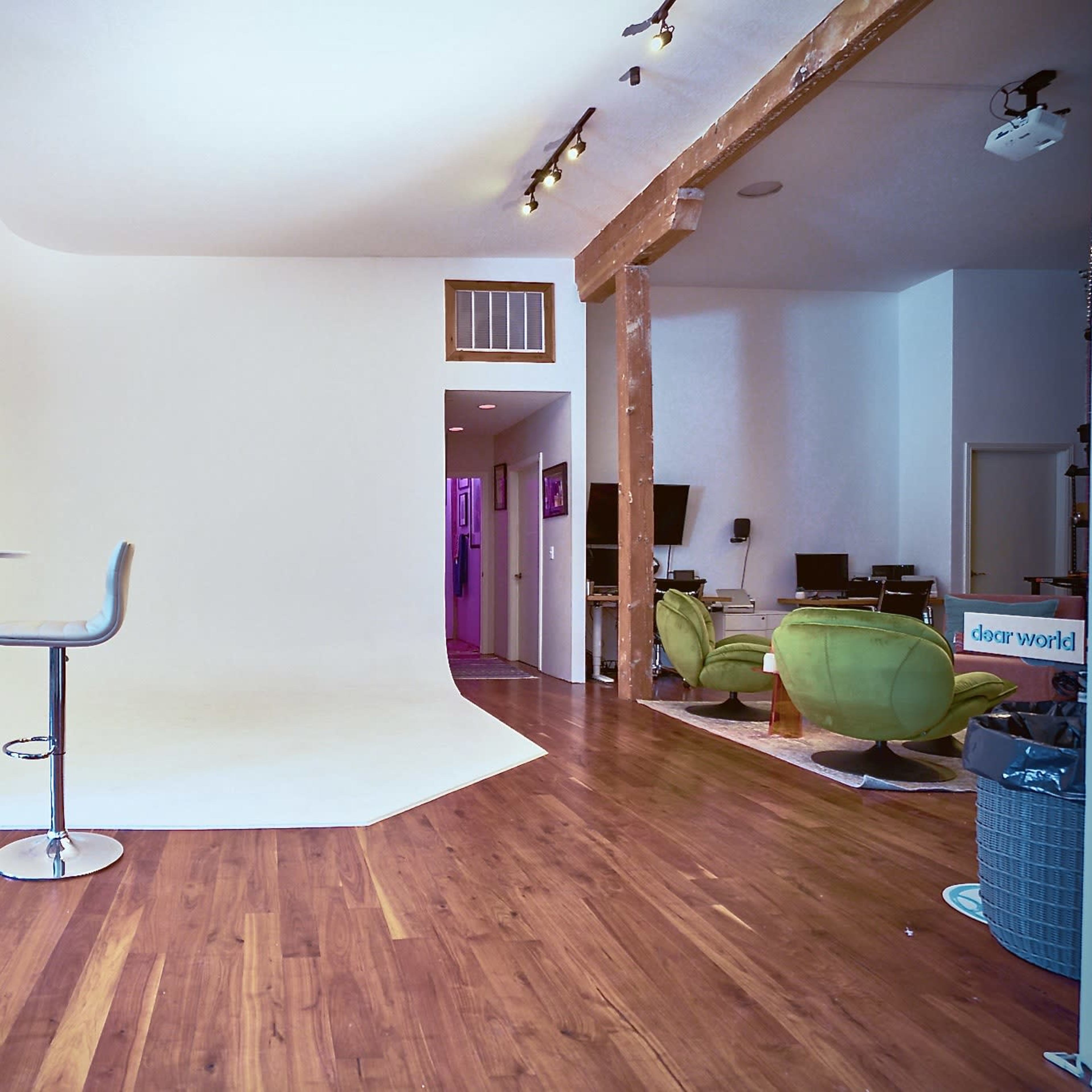 A spacious room with a white backdrop, two modern bar stools at a round table, and distinct areas featuring green chairs and various decor.
