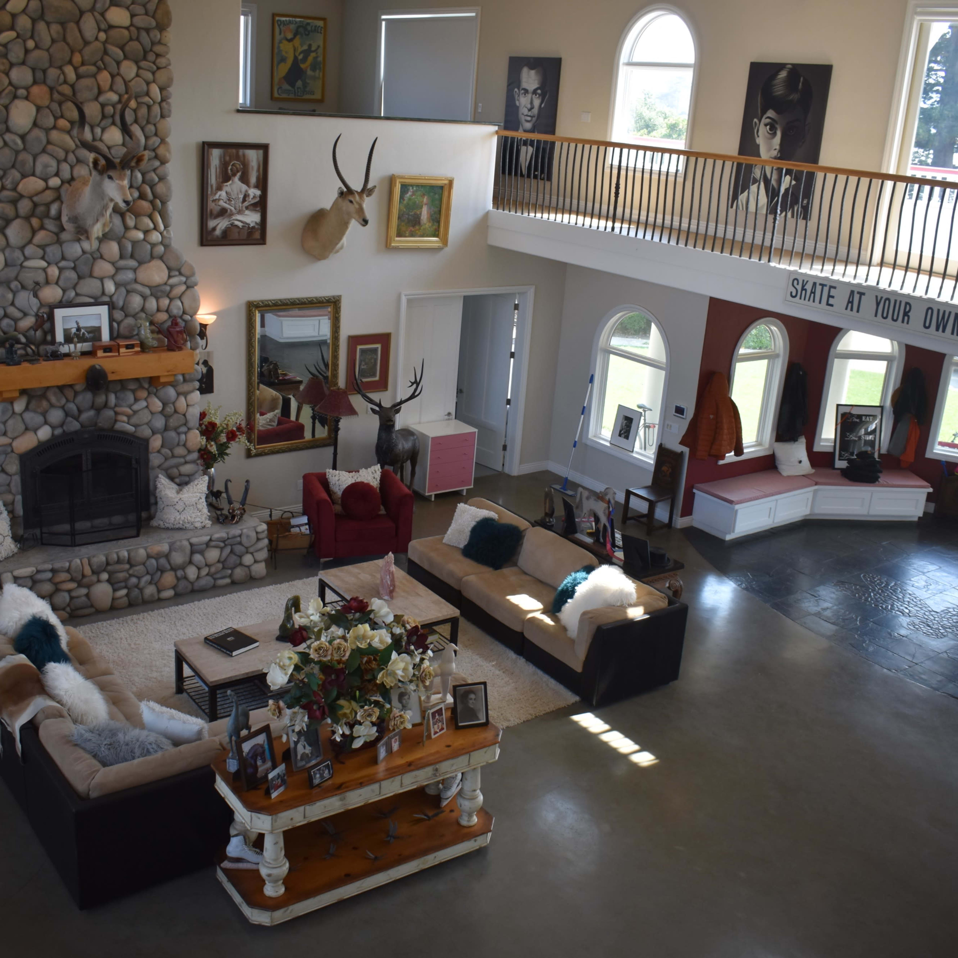 A spacious living area featuring a large stone fireplace, elevated seating areas, and various framed artworks displayed on the walls.