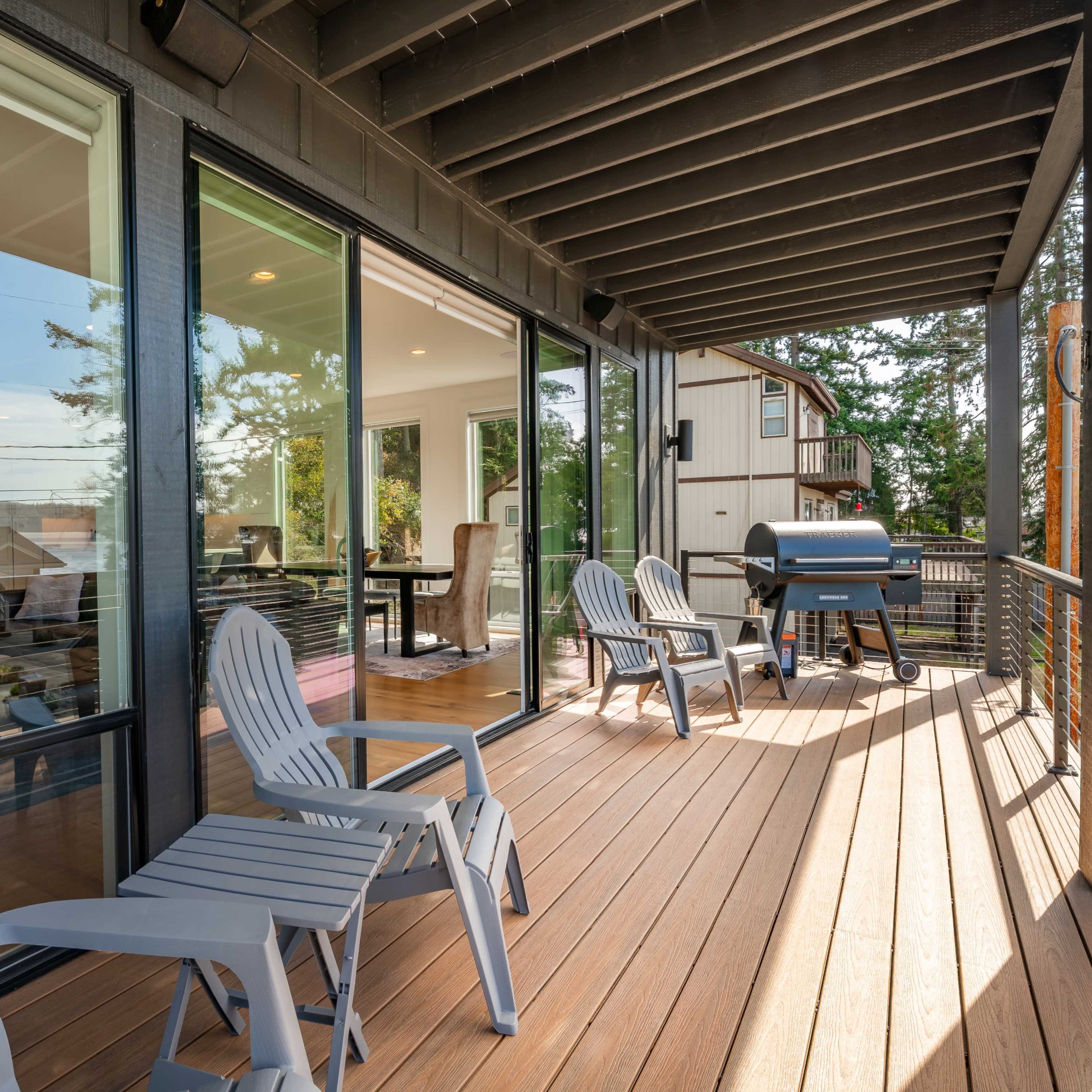 A deck with light-colored chairs and a grill overlooks a neighborhood through large glass doors.