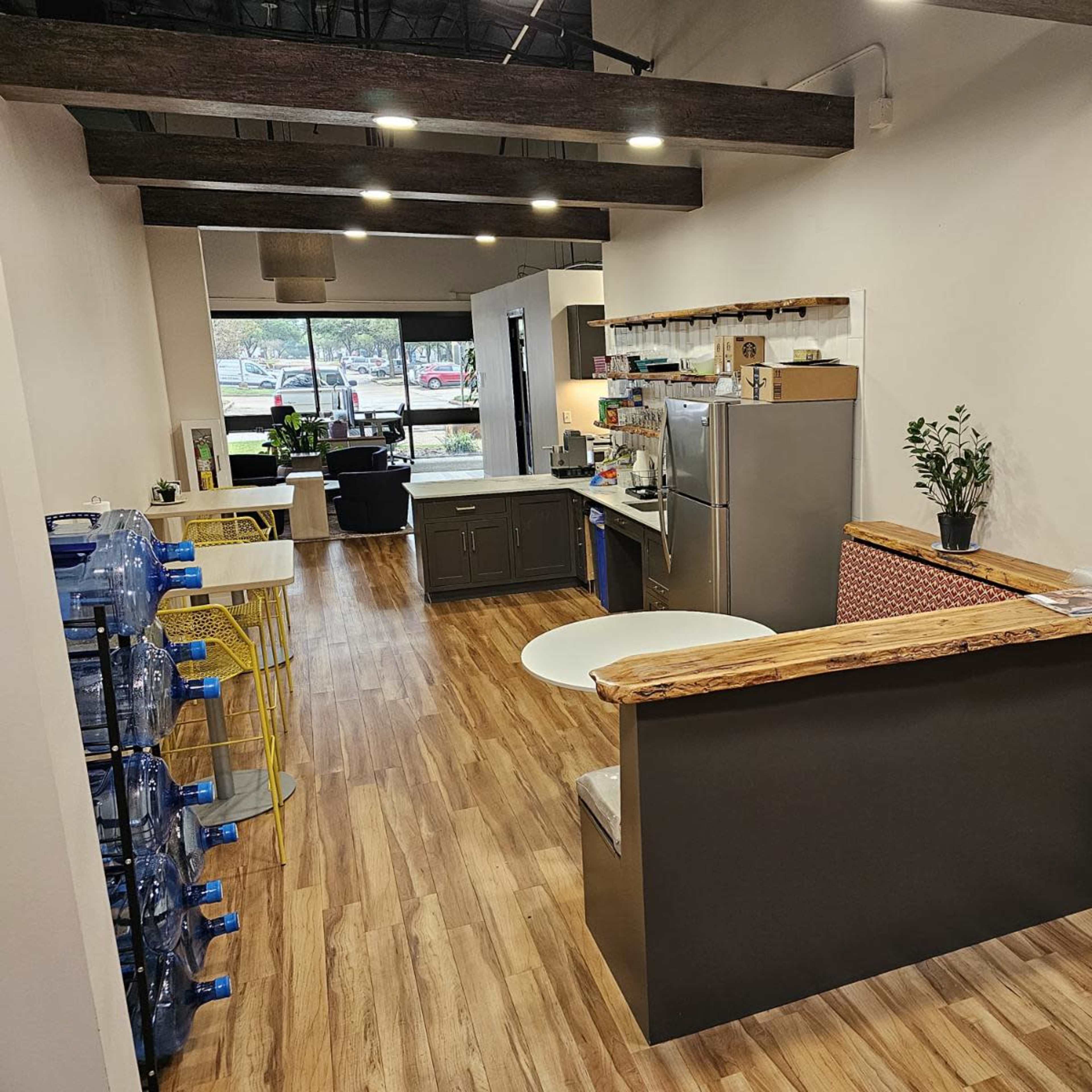 A modern office kitchen area with a counter, appliances, and seating, adjacent to an open workspace.