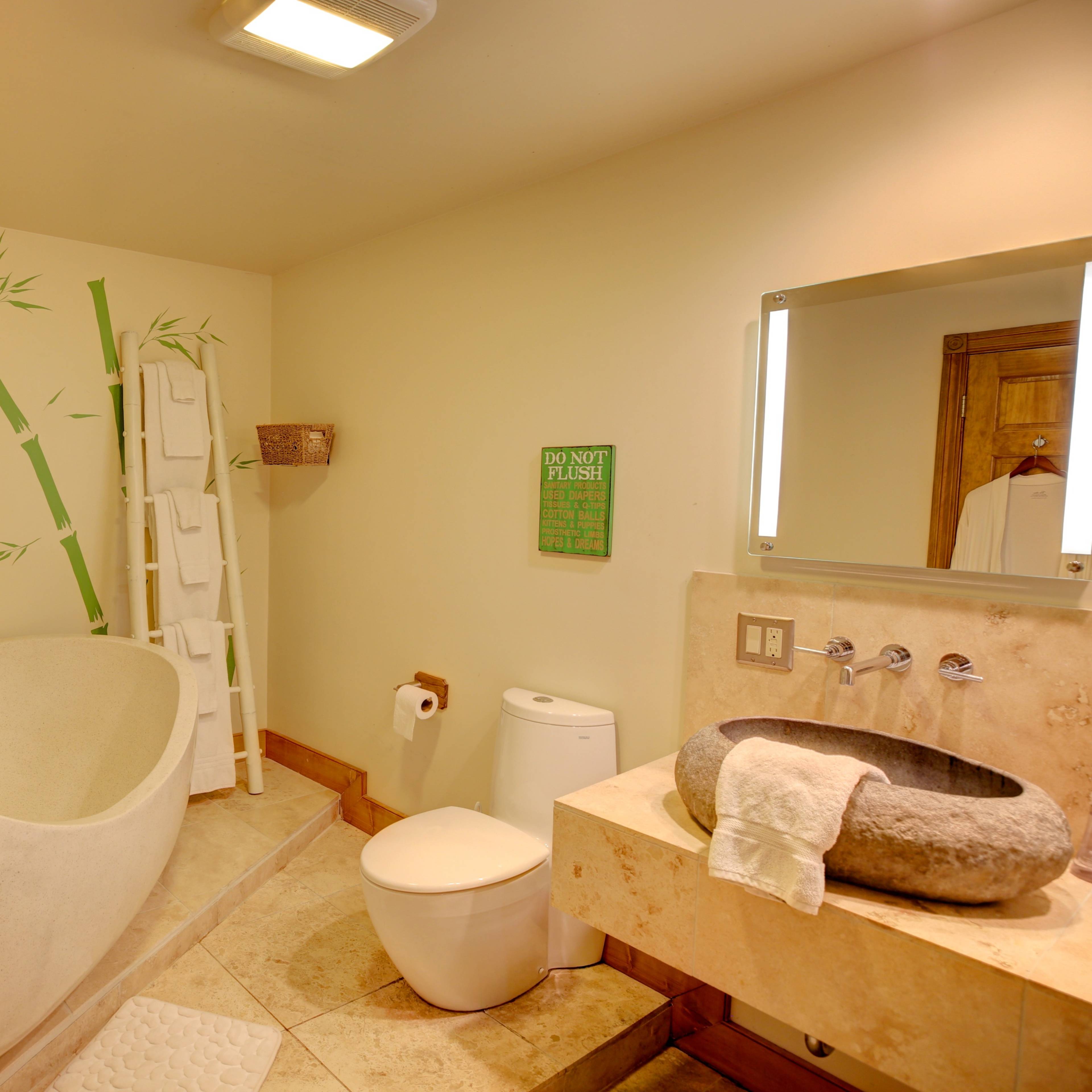 The bathroom features a freestanding tub, a modern toilet, a stone sink, and bamboo wall decor.