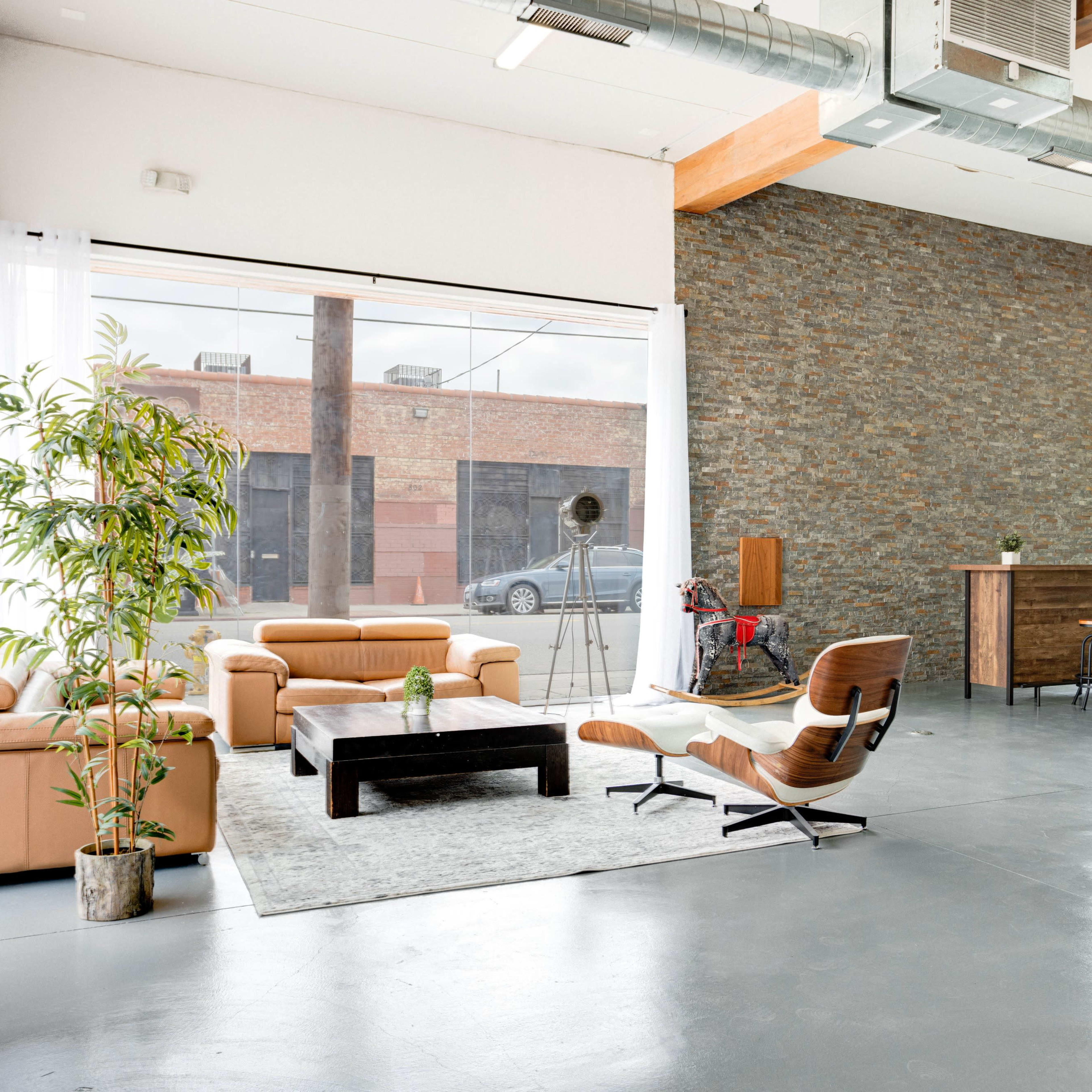 A spacious interior featuring a seating area with a tan leather sofa, a wooden bar, a decorative plant, and large windows that open to an outdoor view.