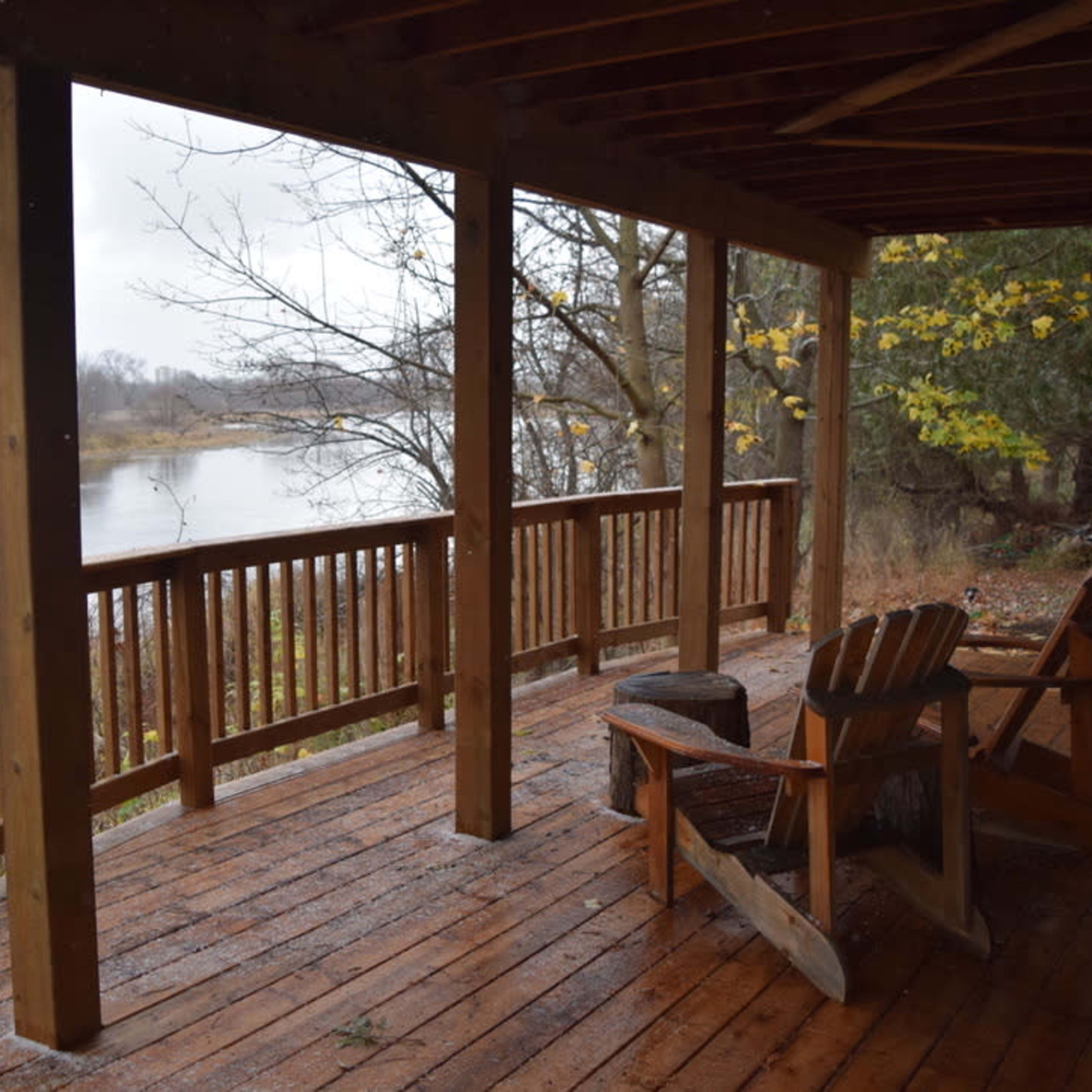 A wooden deck with two chairs overlooks a calm river surrounded by bare trees and autumn foliage.