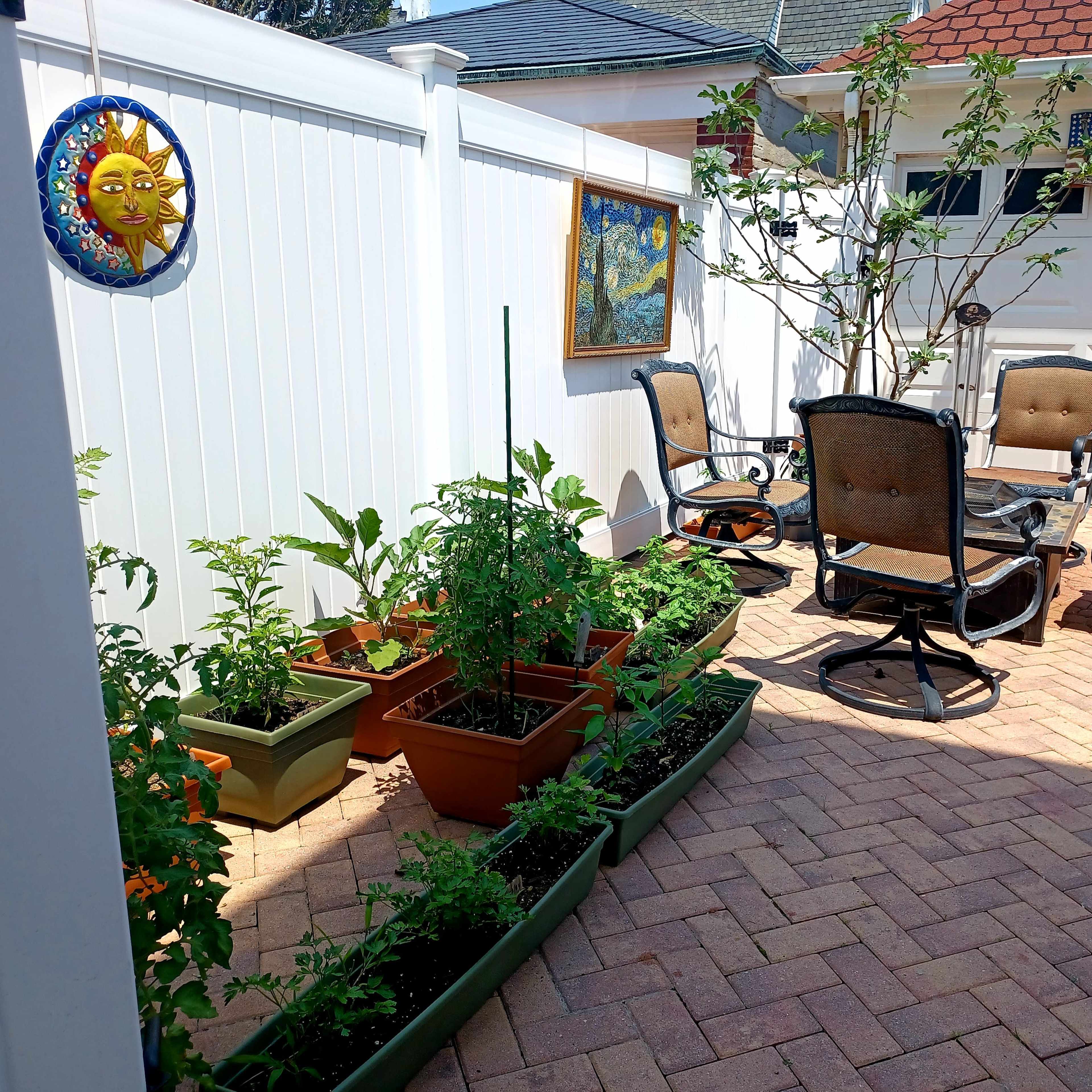 A patio area with potted plants and a seating arrangement, surrounded by a white fence and a garage door in the background.