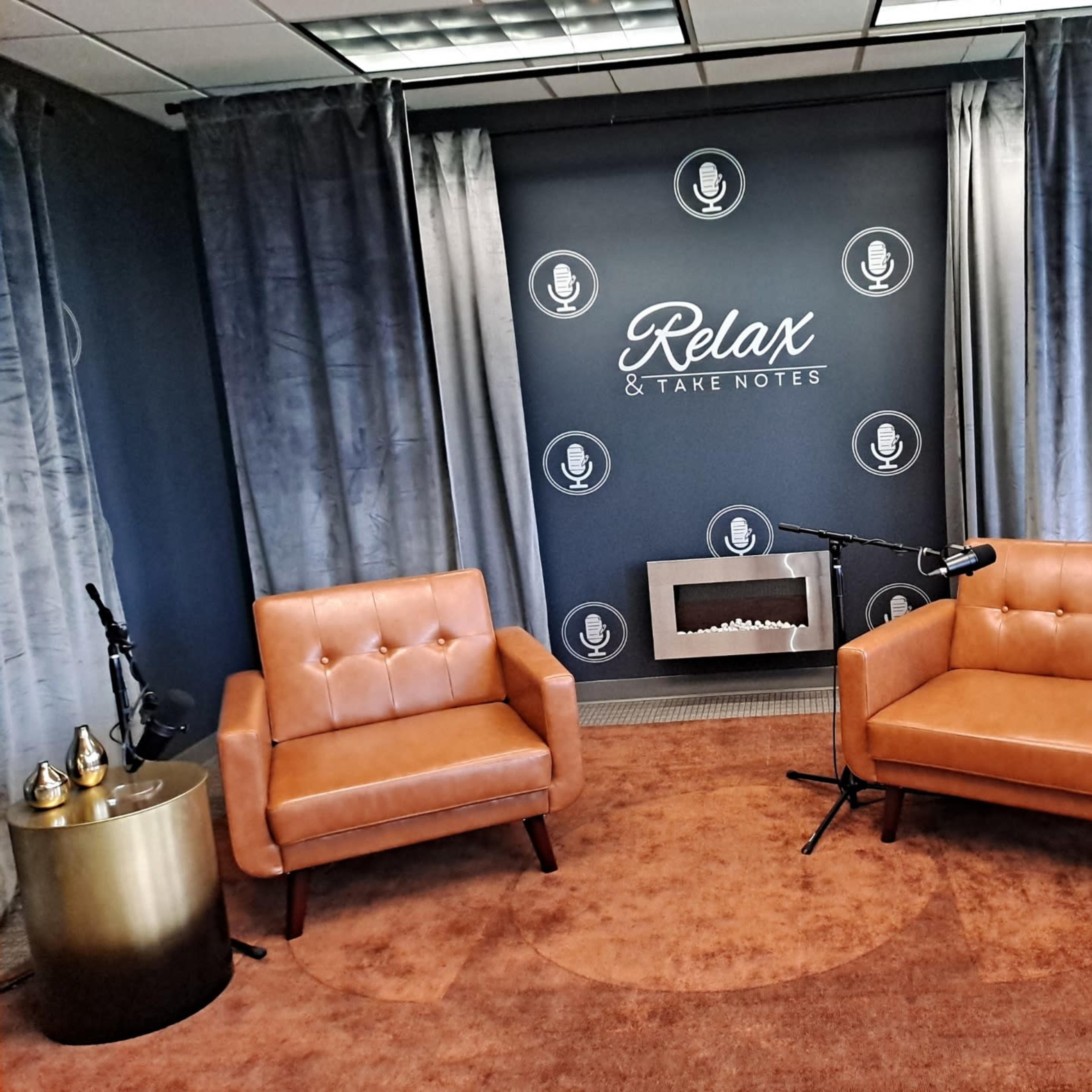 A cozy indoor setting with two brown leather chairs, a small golden side table on each side, a decorative wall featuring microphones, and a modern fireplace.