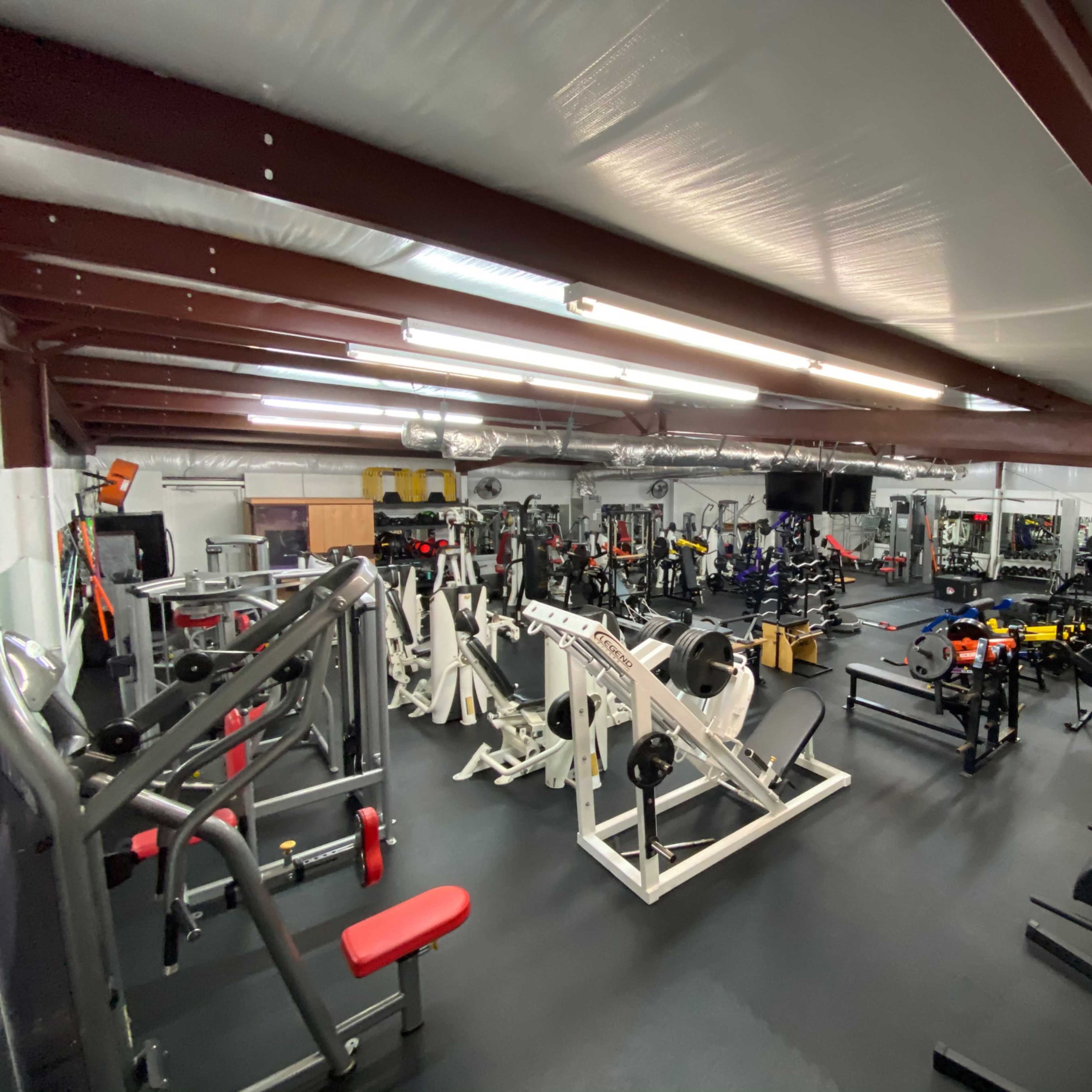 A spacious gym interior filled with various exercise equipment, including weight machines, free weights, and cardio stations.