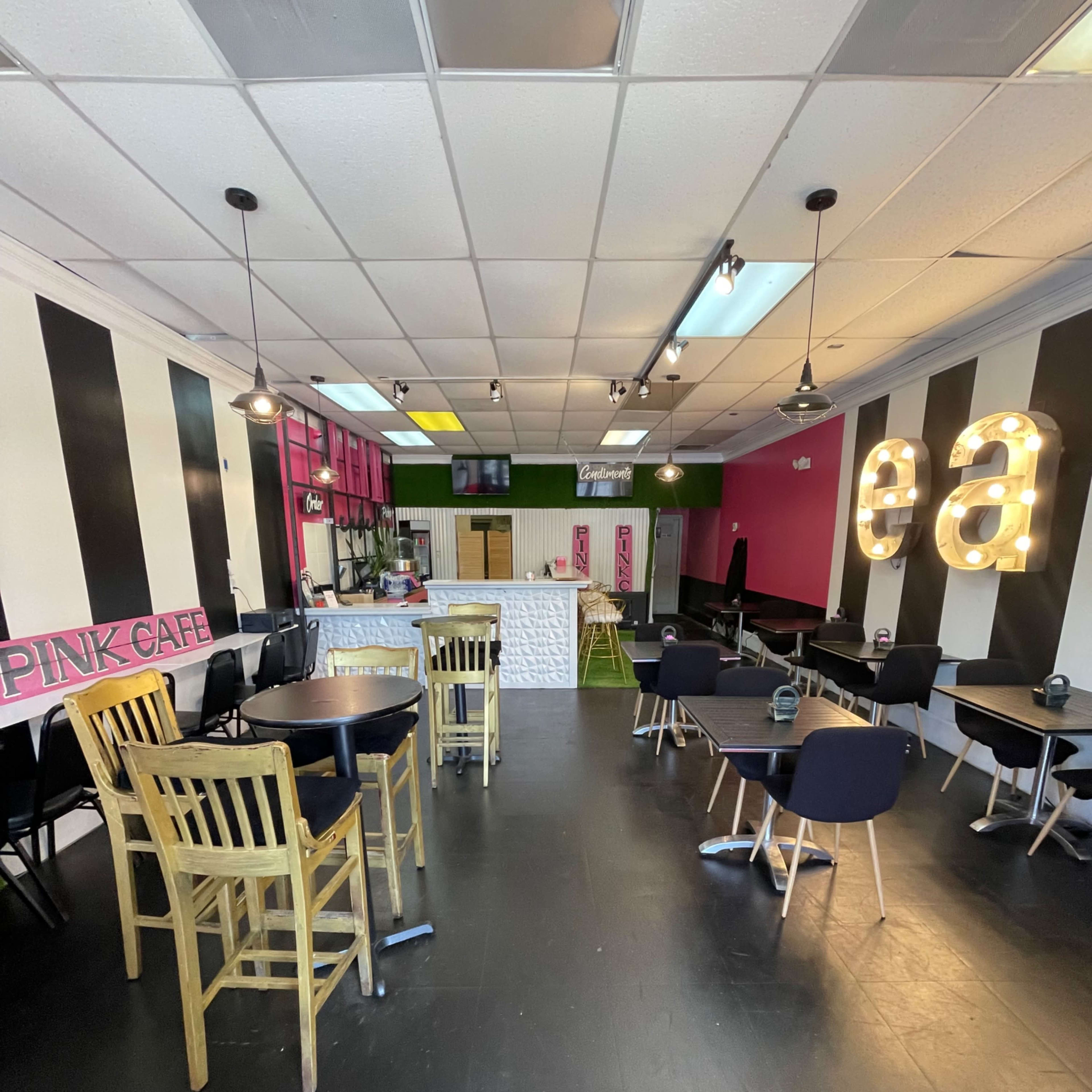 The interior of a cafe featuring a mix of black and white striped walls, wooden tables, and chairs, with a brightly colored backdrop and illuminated signs.