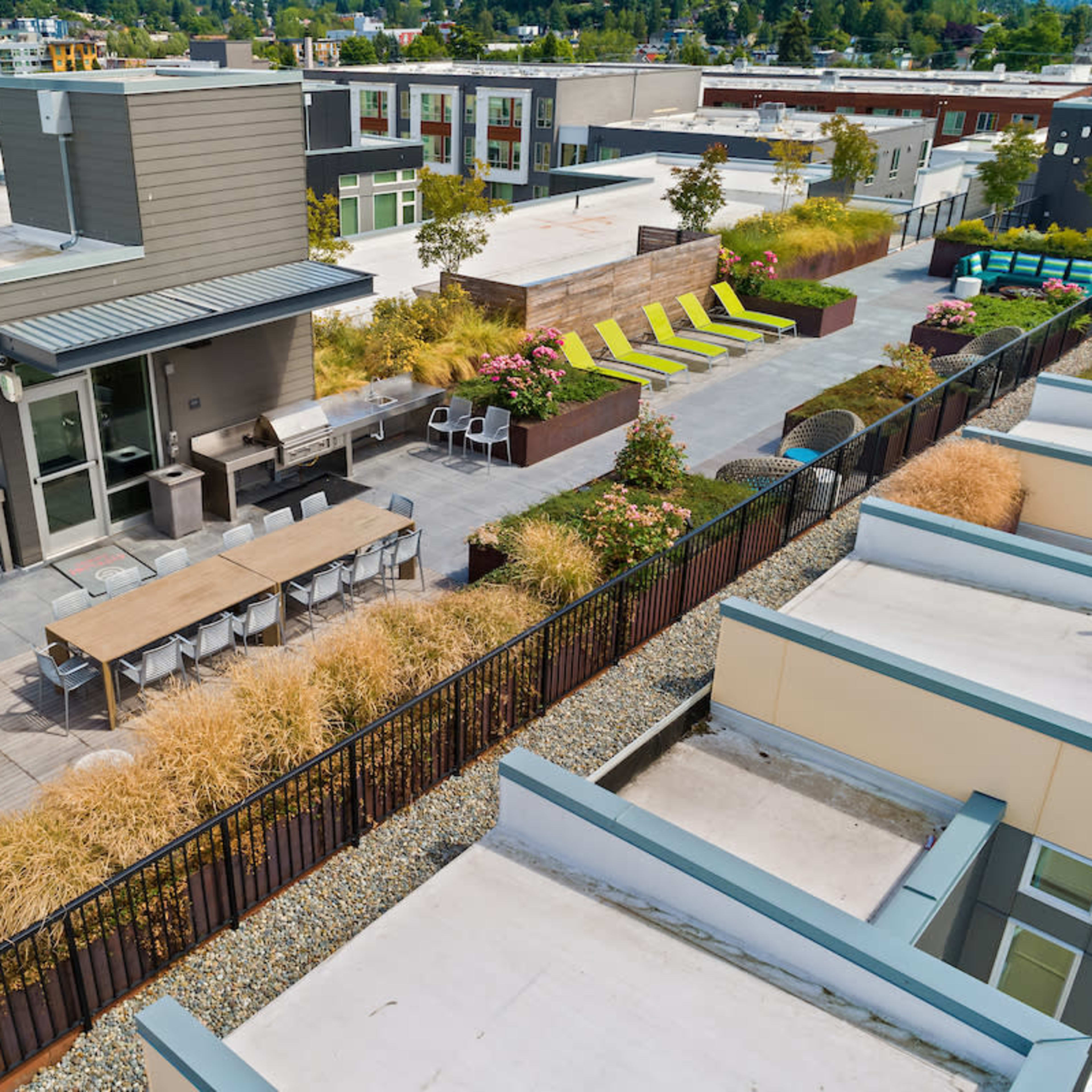 A rooftop terrace featuring seating areas, lounge chairs, and landscaping with various plants and flowers.