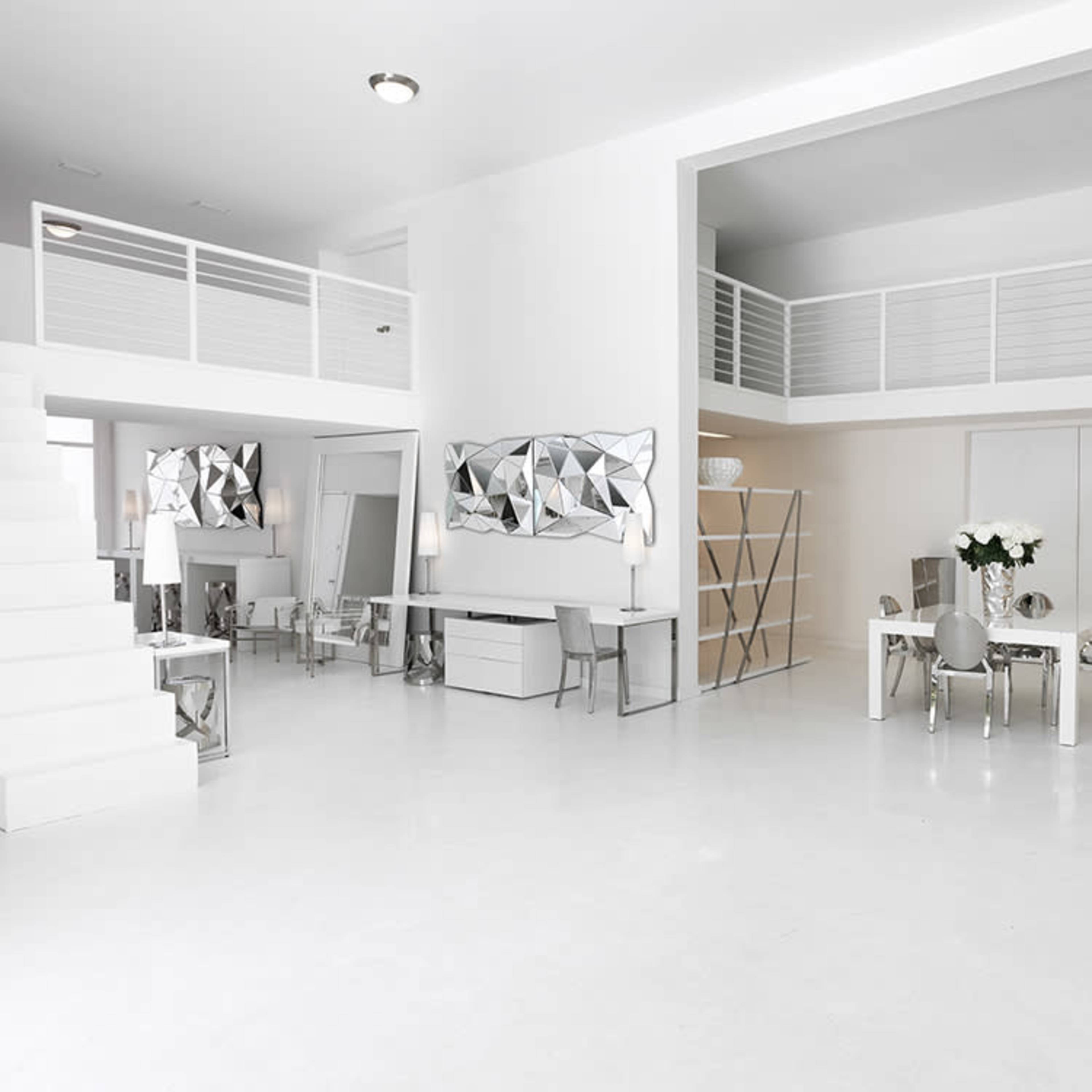 A modern, spacious interior with a white color scheme, featuring a dining area, a staircase, and a lofted section above.