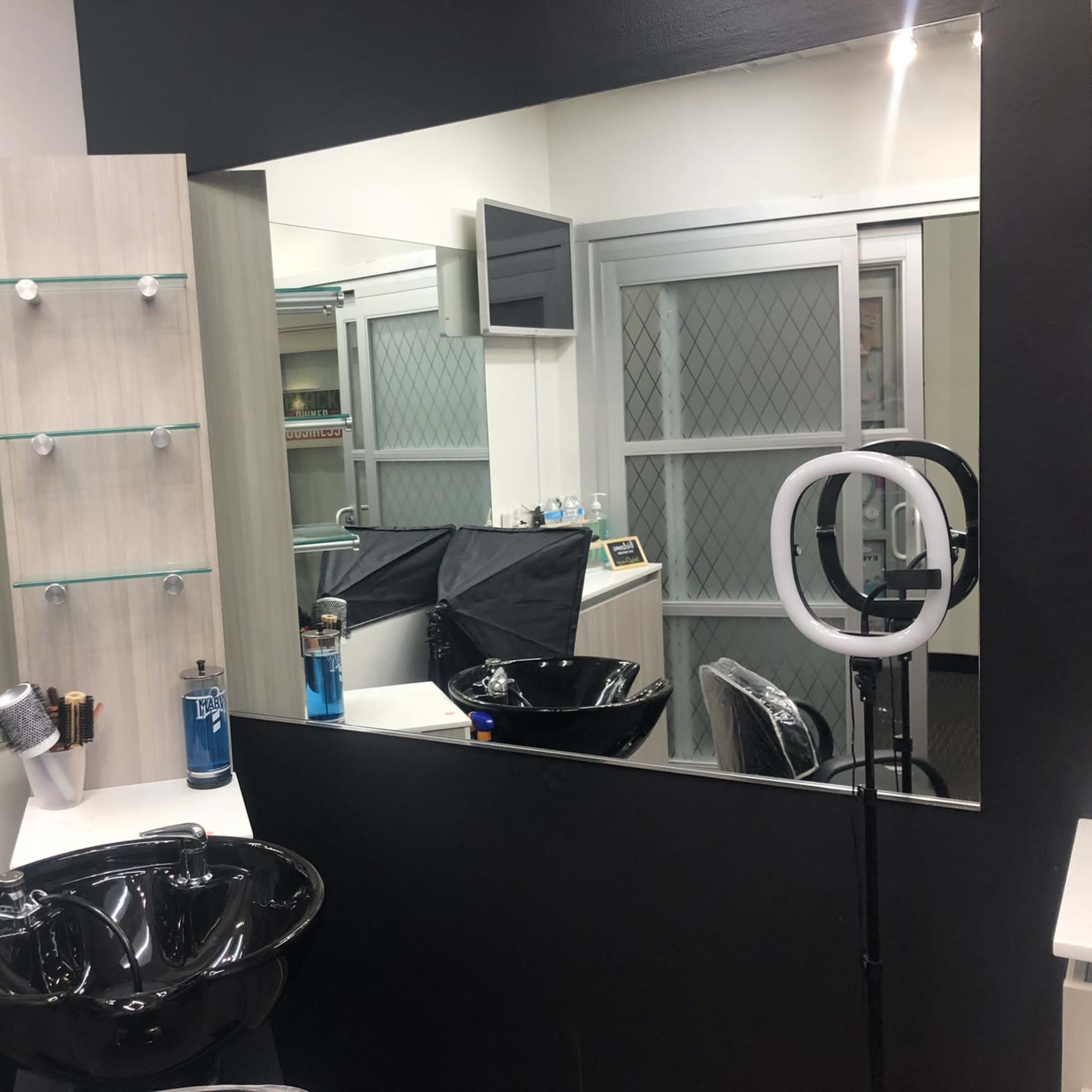 A hair salon interior featuring a black sink, mirrors, and a ring light setup in a well-lit space.