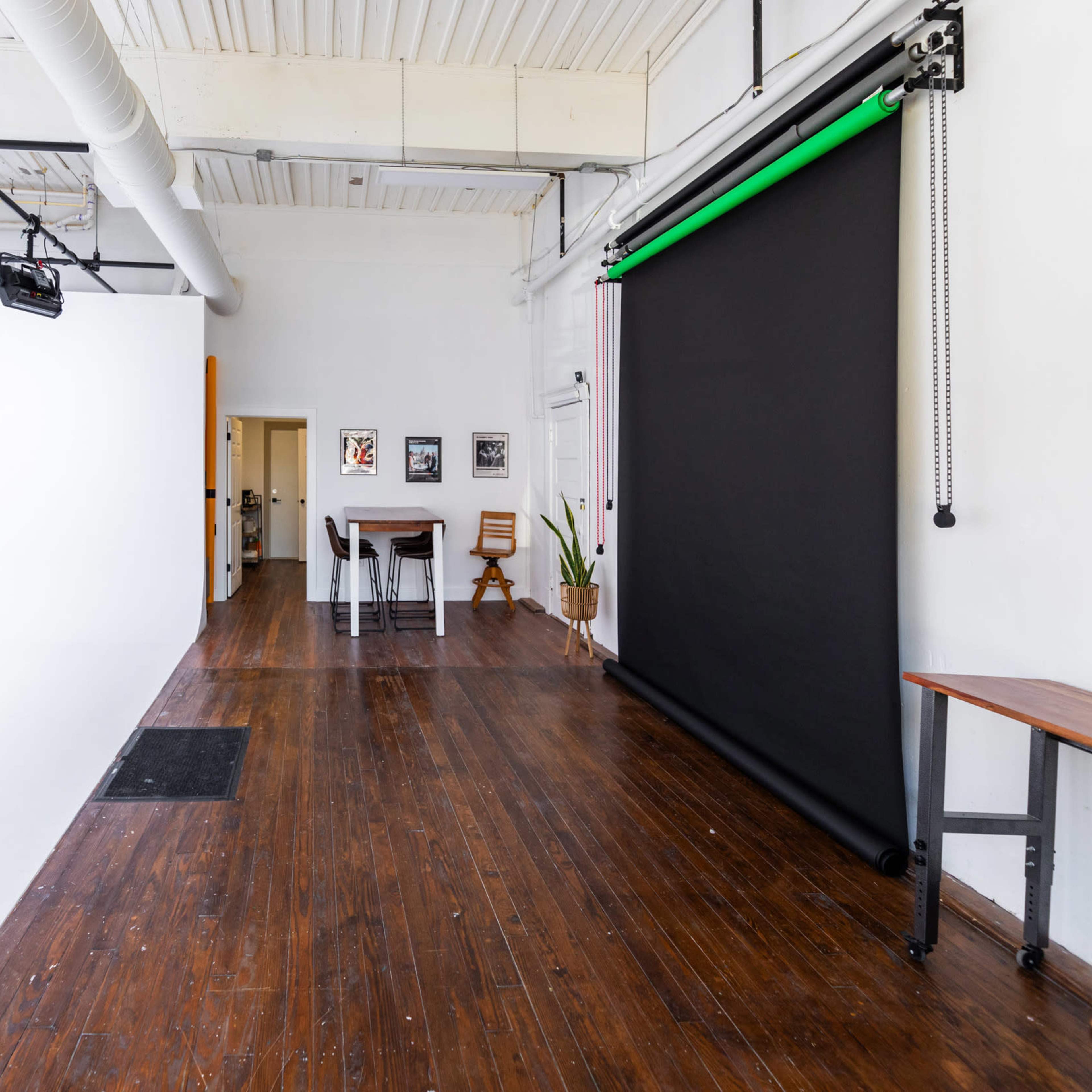 A spacious studio with wooden flooring, white walls, and a black backdrop setup along one side.