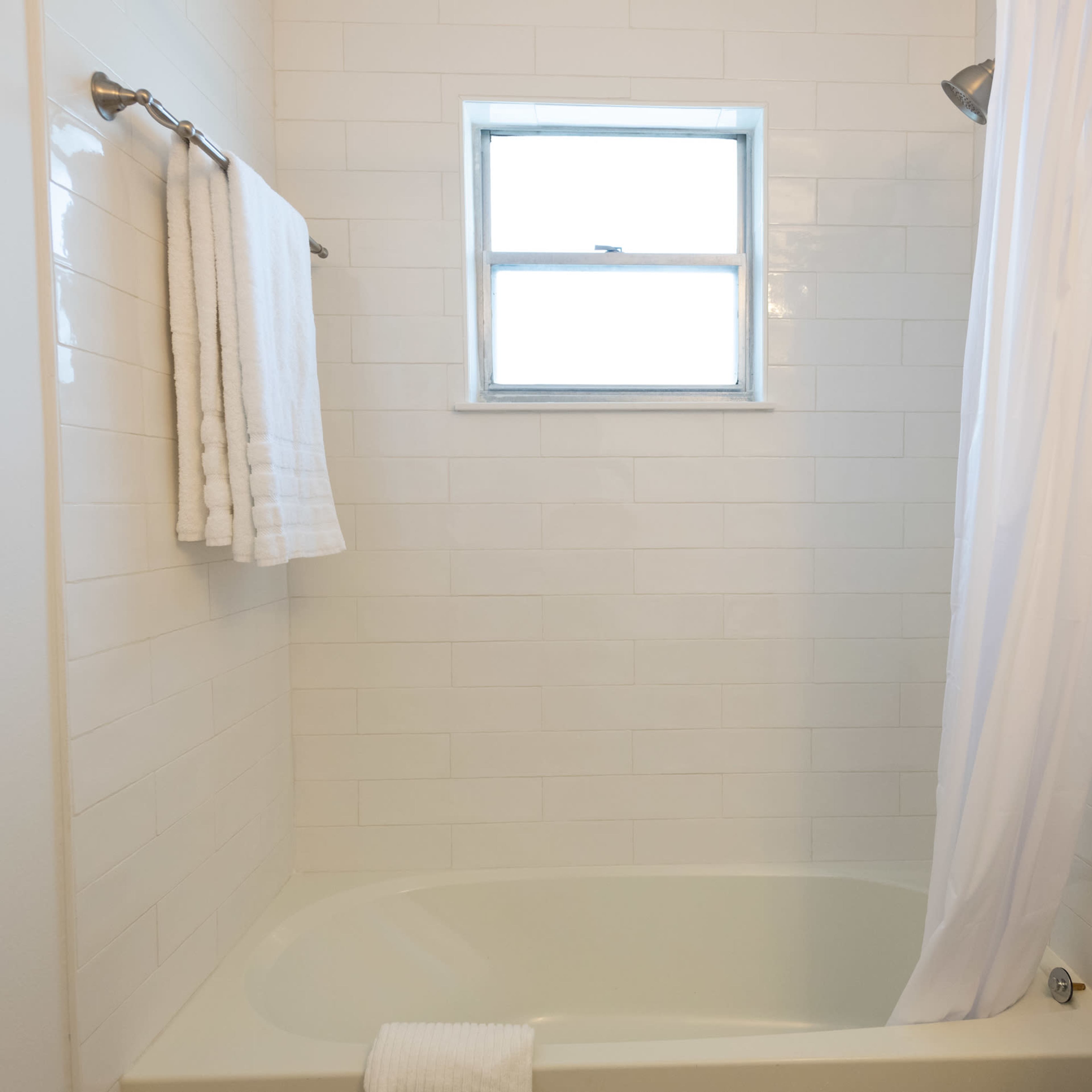 A clean bathroom with a bathtub, a shower curtain, and white towels hanging on a rack.
