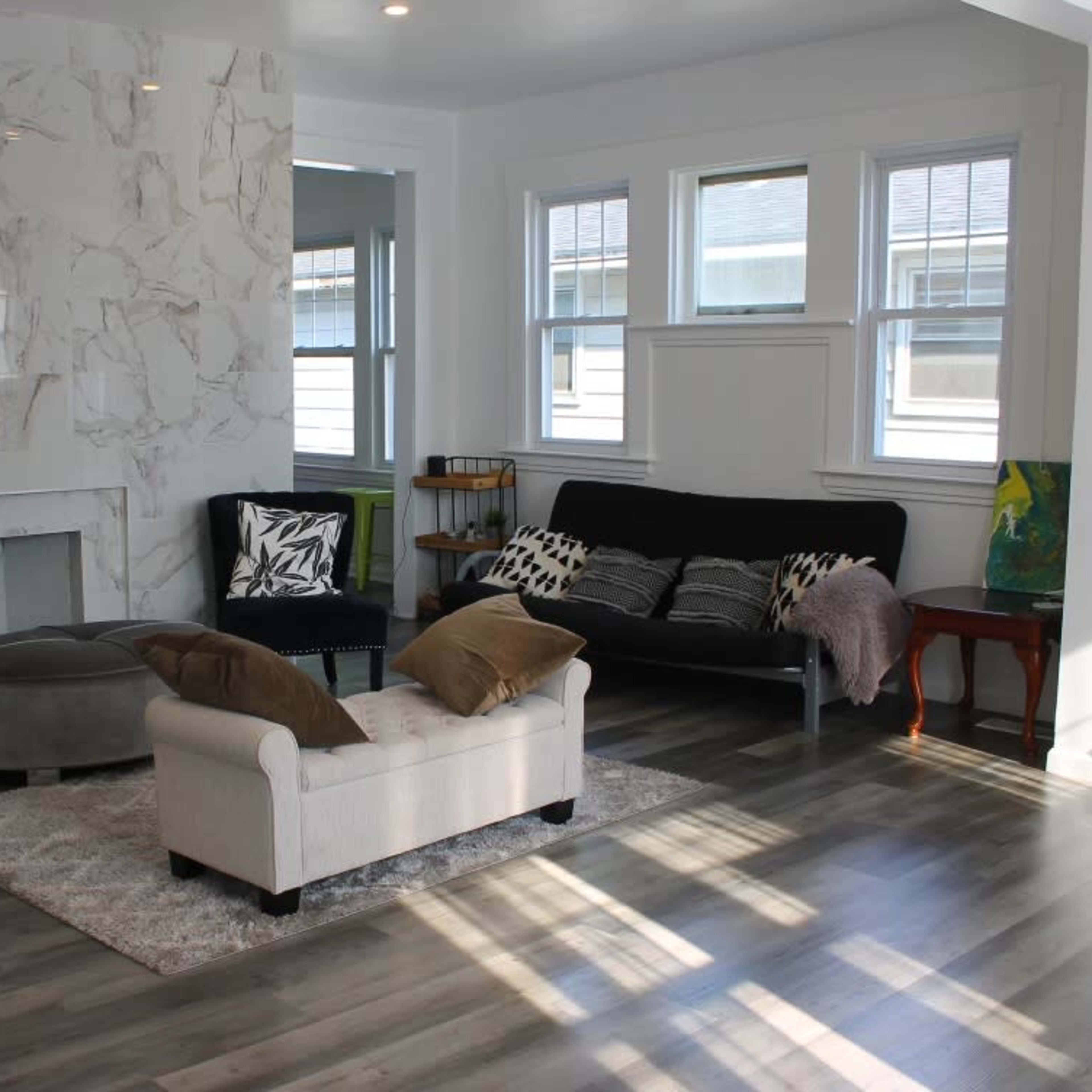 A modern living room with light wood flooring, a marble accent wall, a seating area consisting of a sofa and two chairs, and a small side table.